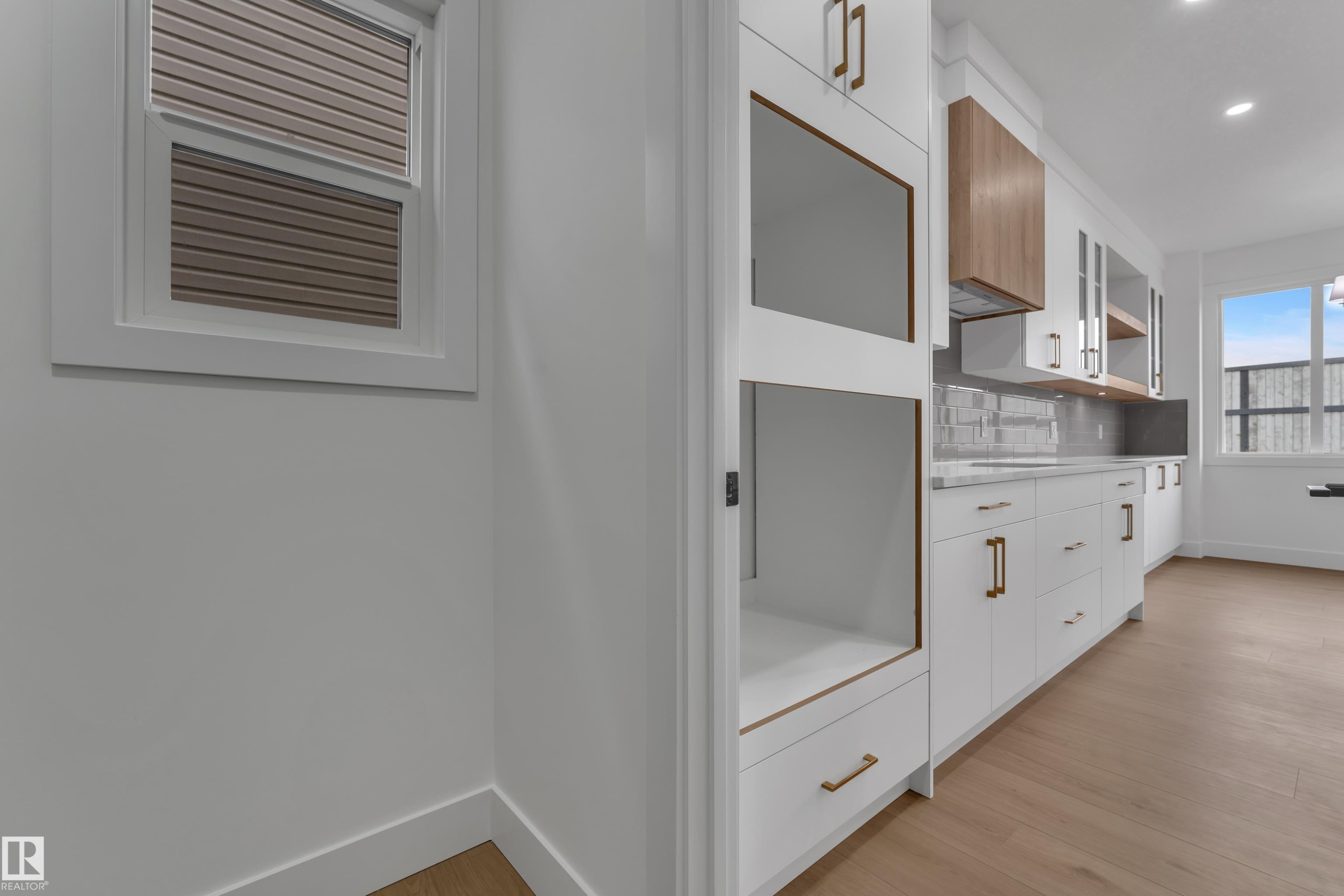 White custom cabinetry with integrated appliance spaces, gold-tone hardware, wood-finish flooring, and a tile backsplash - 178 Munn Way, Leduc, AB