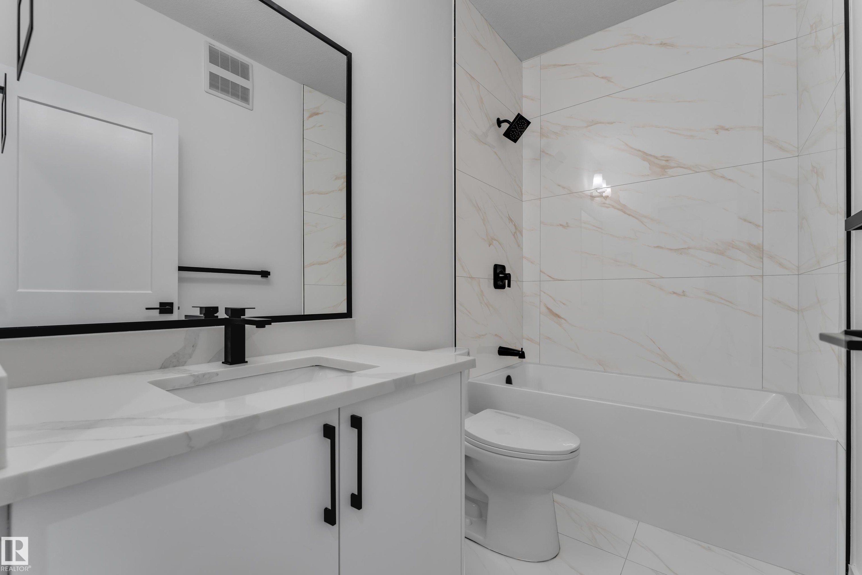 Bathroom featuring a white vanity with an integrated sink, matte black fixtures, a rectangular mirror, and a bathtub with tile surround - 178 Munn Way, Leduc, AB