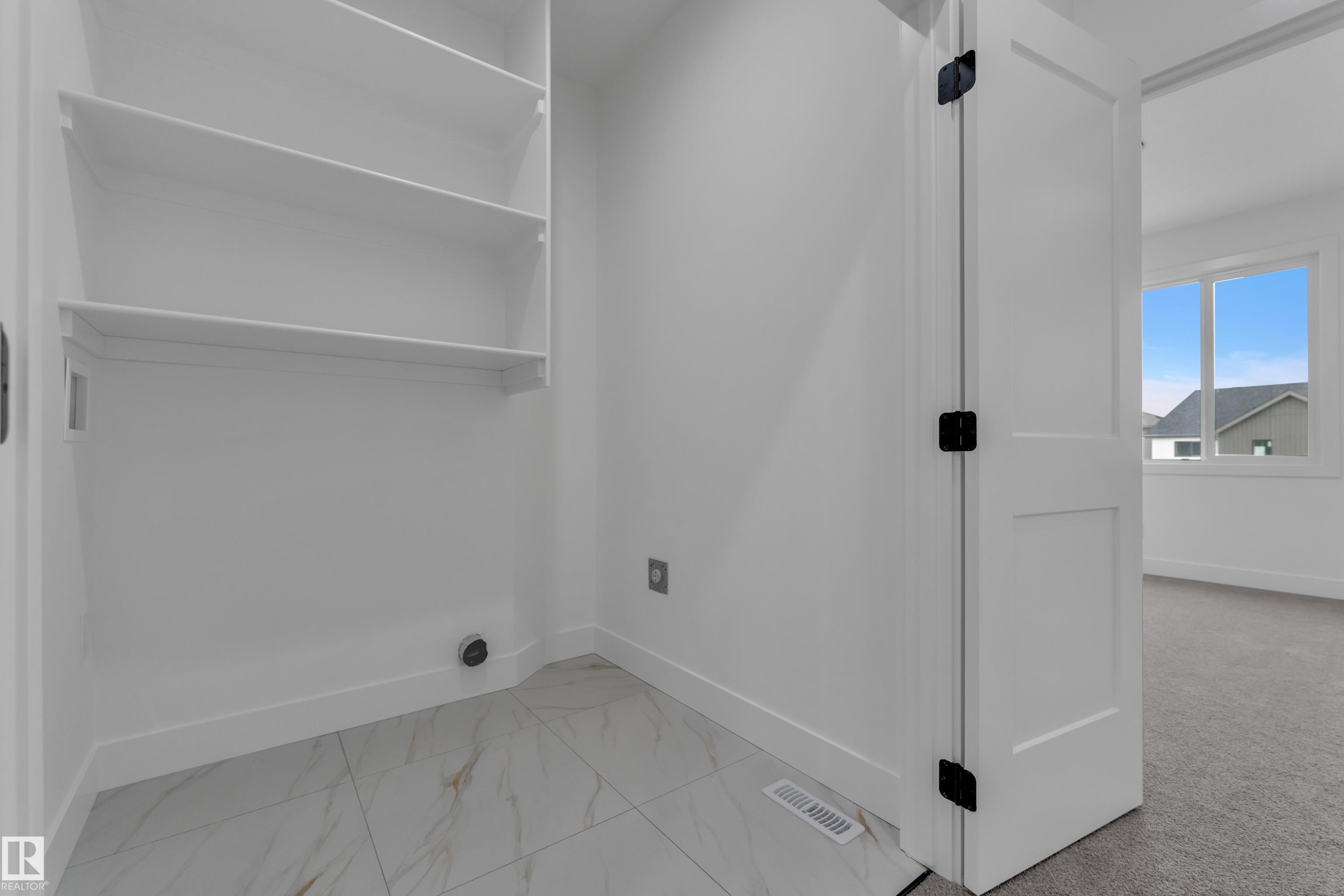 White built-in shelving, white flat-panel door with matte black hardware, and patterned floor tile - 178 Munn Way, Leduc, AB