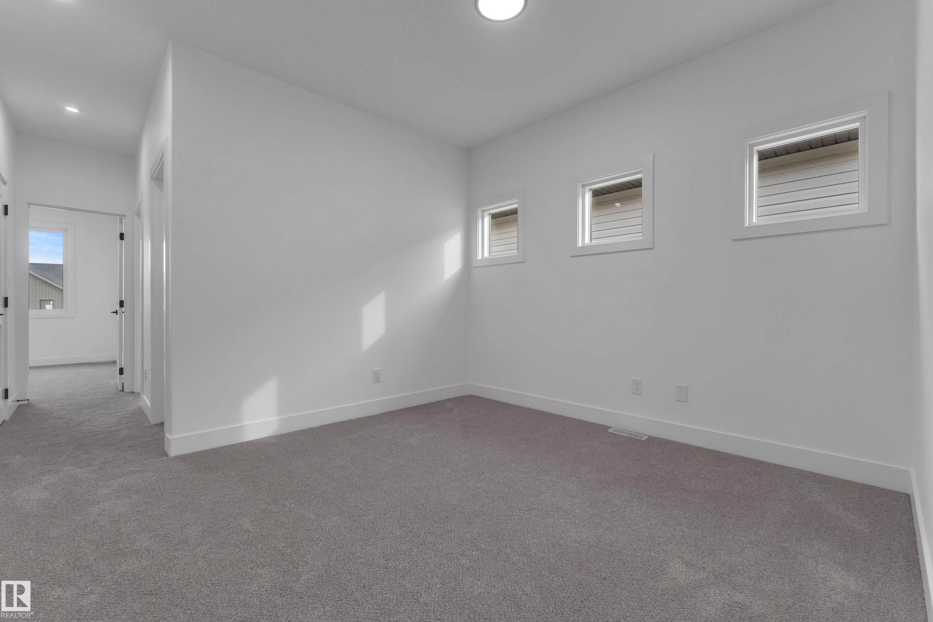 Plush gray carpeting with white walls, three transom windows, a flush-mount ceiling light, and white trim - 178 Munn Way, Leduc, AB