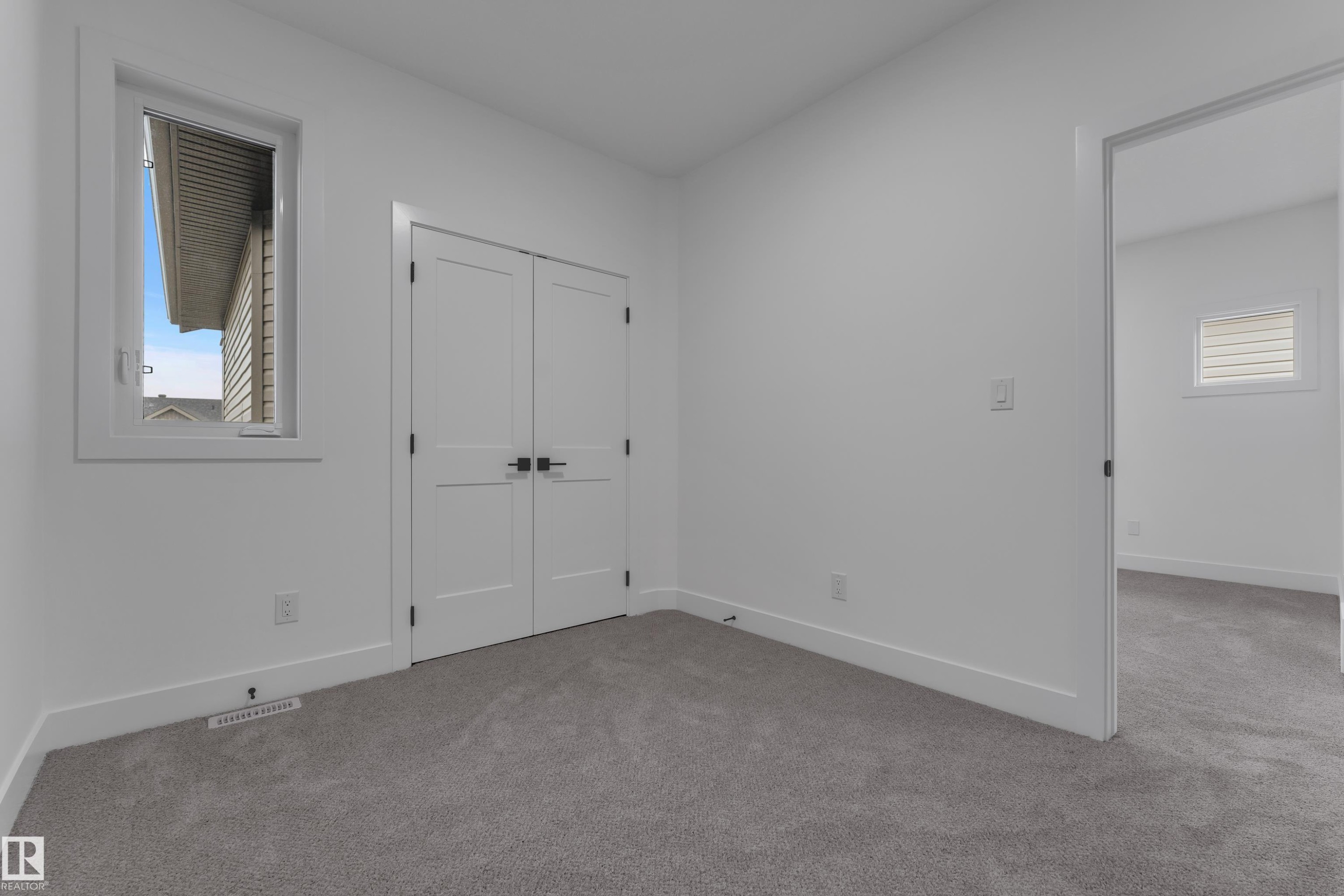 Neutral paint palette with grey carpet, double closet doors with matte black hardware, and a window with white trim - 178 Munn Way, Leduc, AB