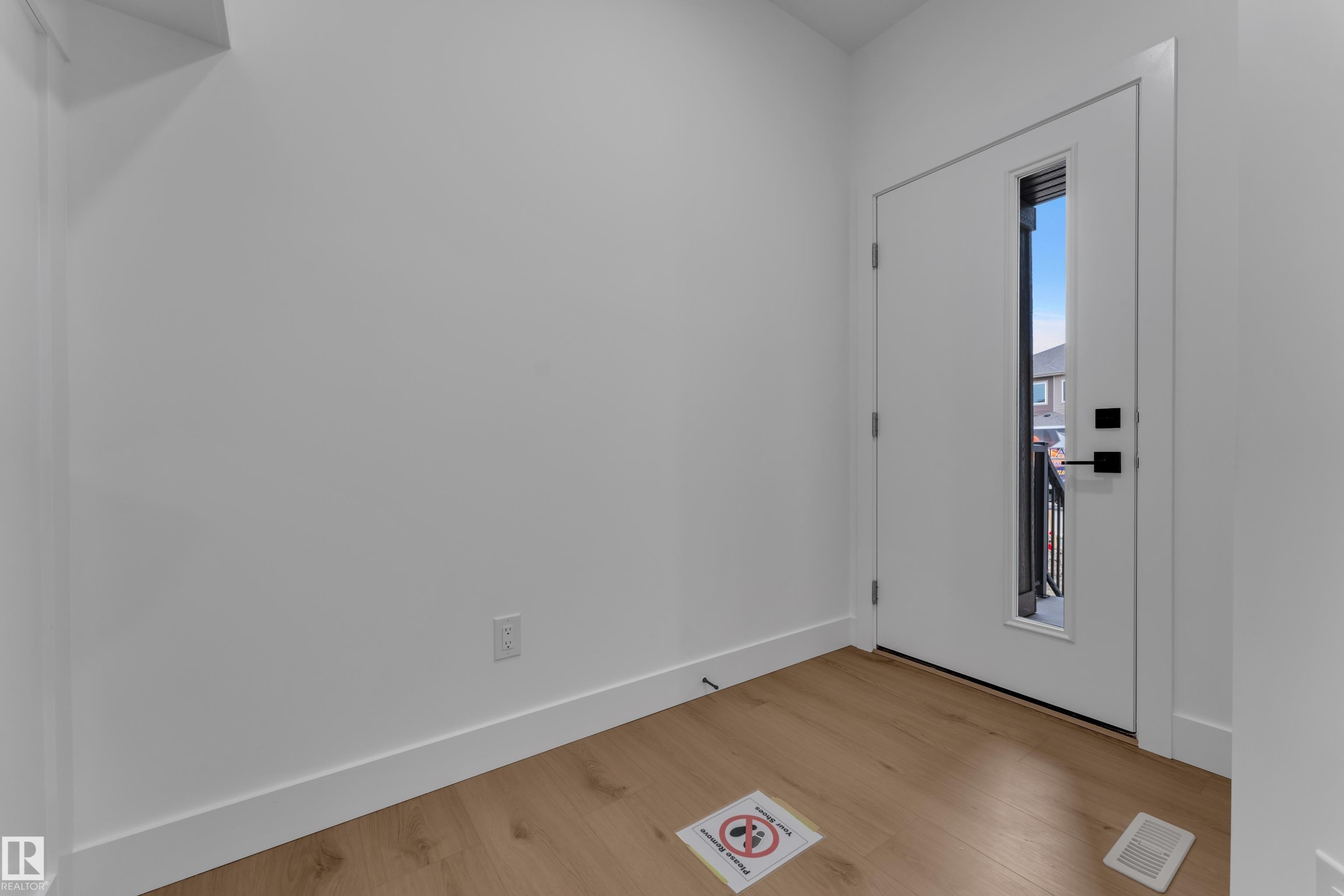 White entry door with a vertical window insert, black hardware, and wood-finish flooring - 178 Munn Way, Leduc, AB