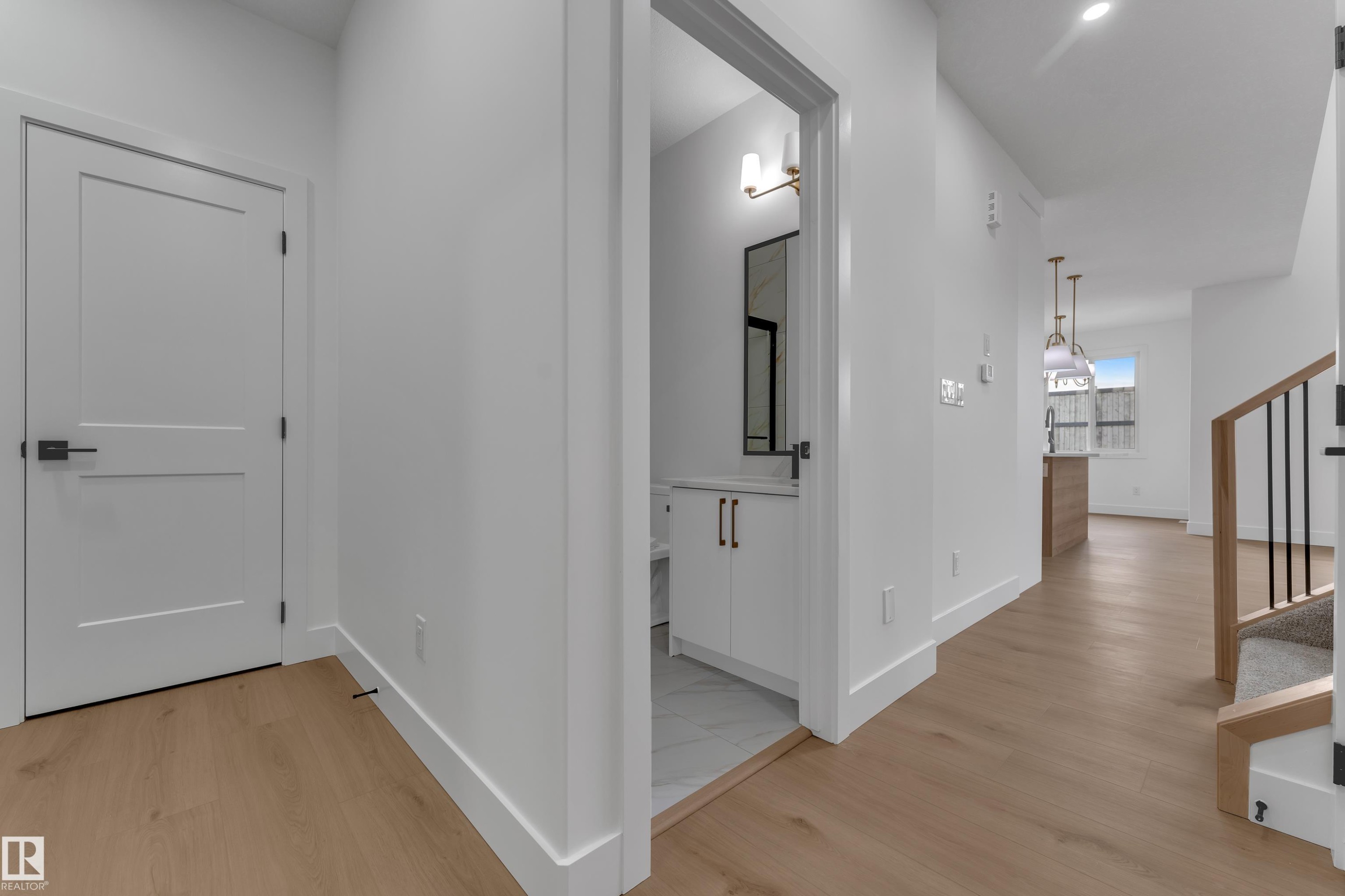 Light wood-finish flooring, white flat panel door with black hardware, white walls, built-in vanity with white cabinetry, and a wood and metal staircase - 178 Munn Way, Leduc, AB