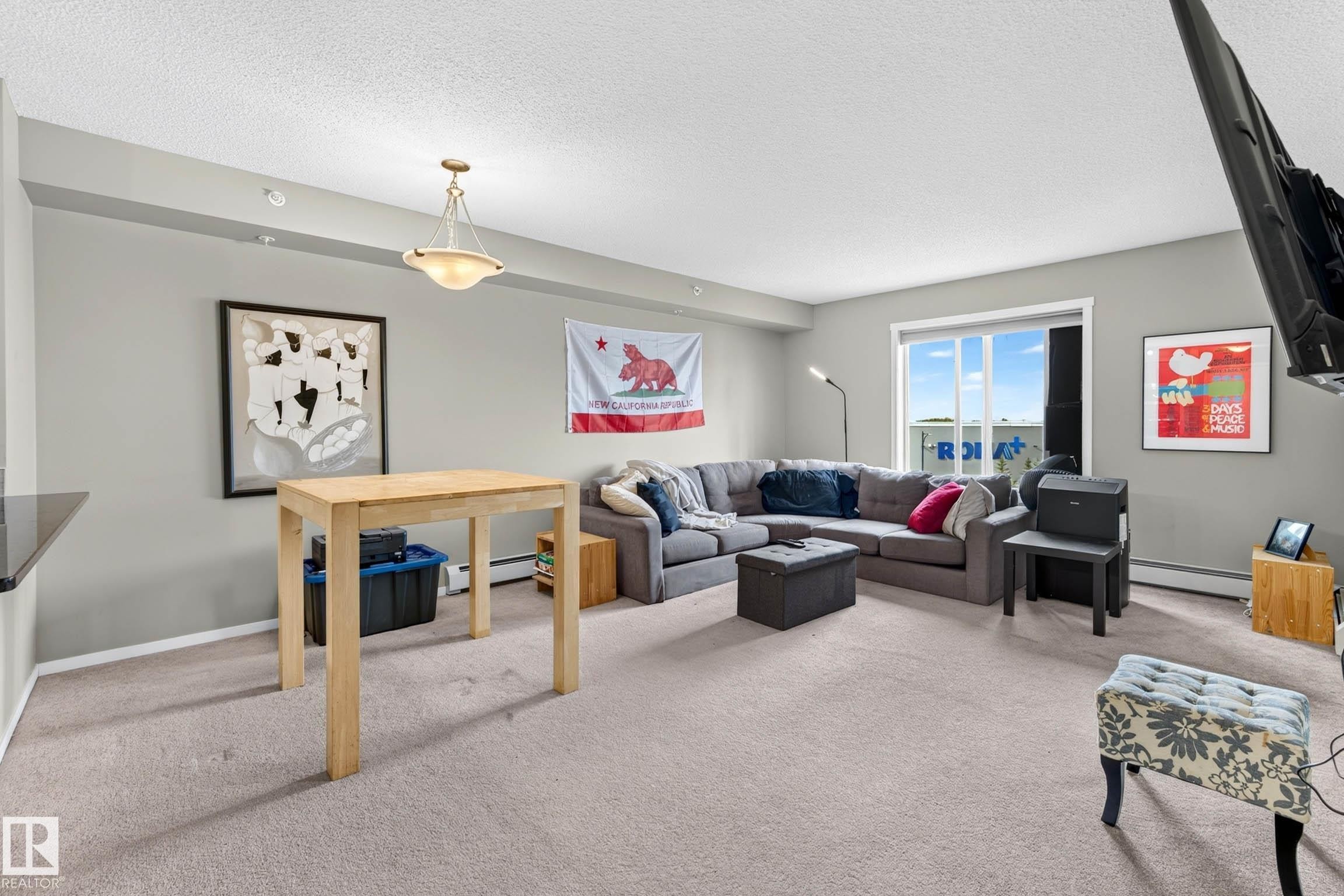 Carpeted living space with light-toned walls, recessed lighting, and a pendant light fixture - #408 25 Element Dr, St. Albert, AB
