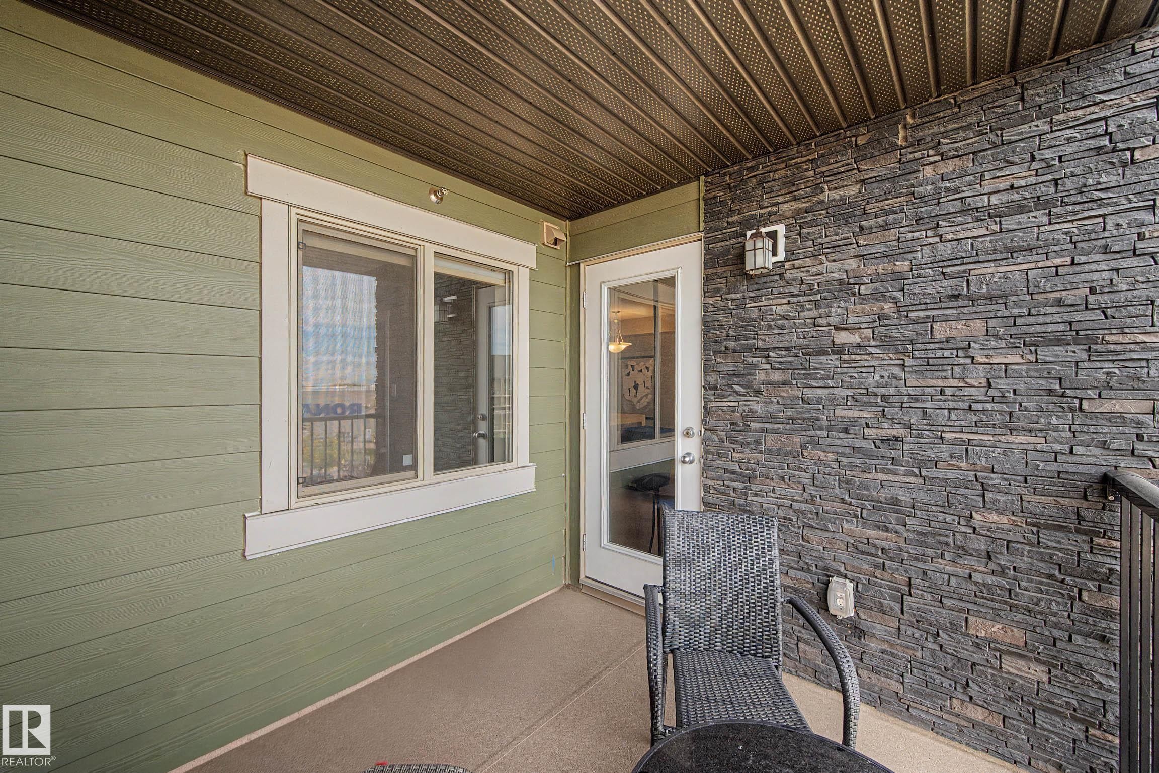 Outdoor balcony featuring a stone veneer accent wall, composite siding, and a solid overhead covering - #408 25 Element Dr, St. Albert, AB
