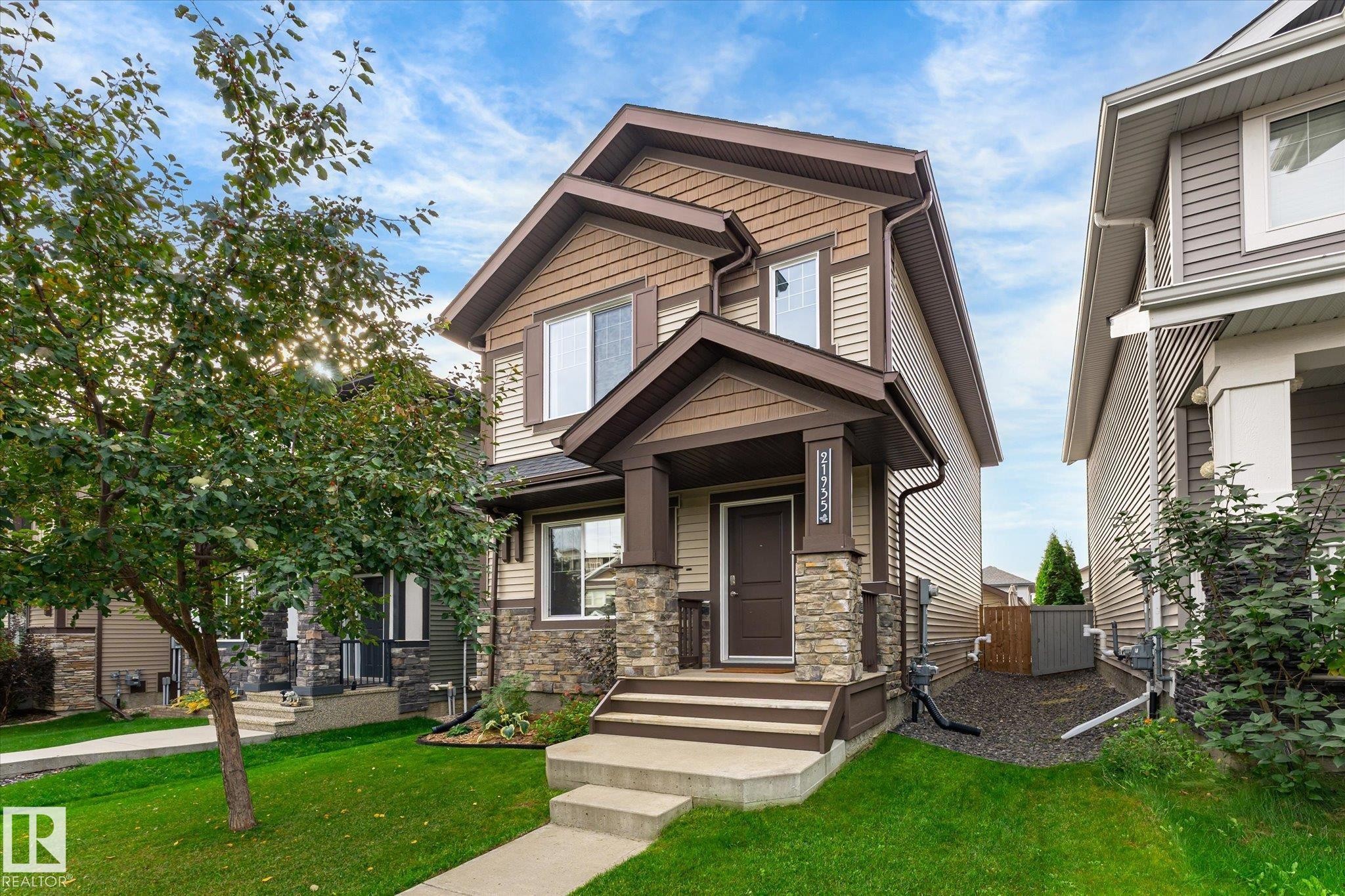 Two-story residence featuring a covered entry, stone column accents, multi-tone siding, and a well-maintained front lawn - 21935 91 Avenue Nw, Edmonton, AB
