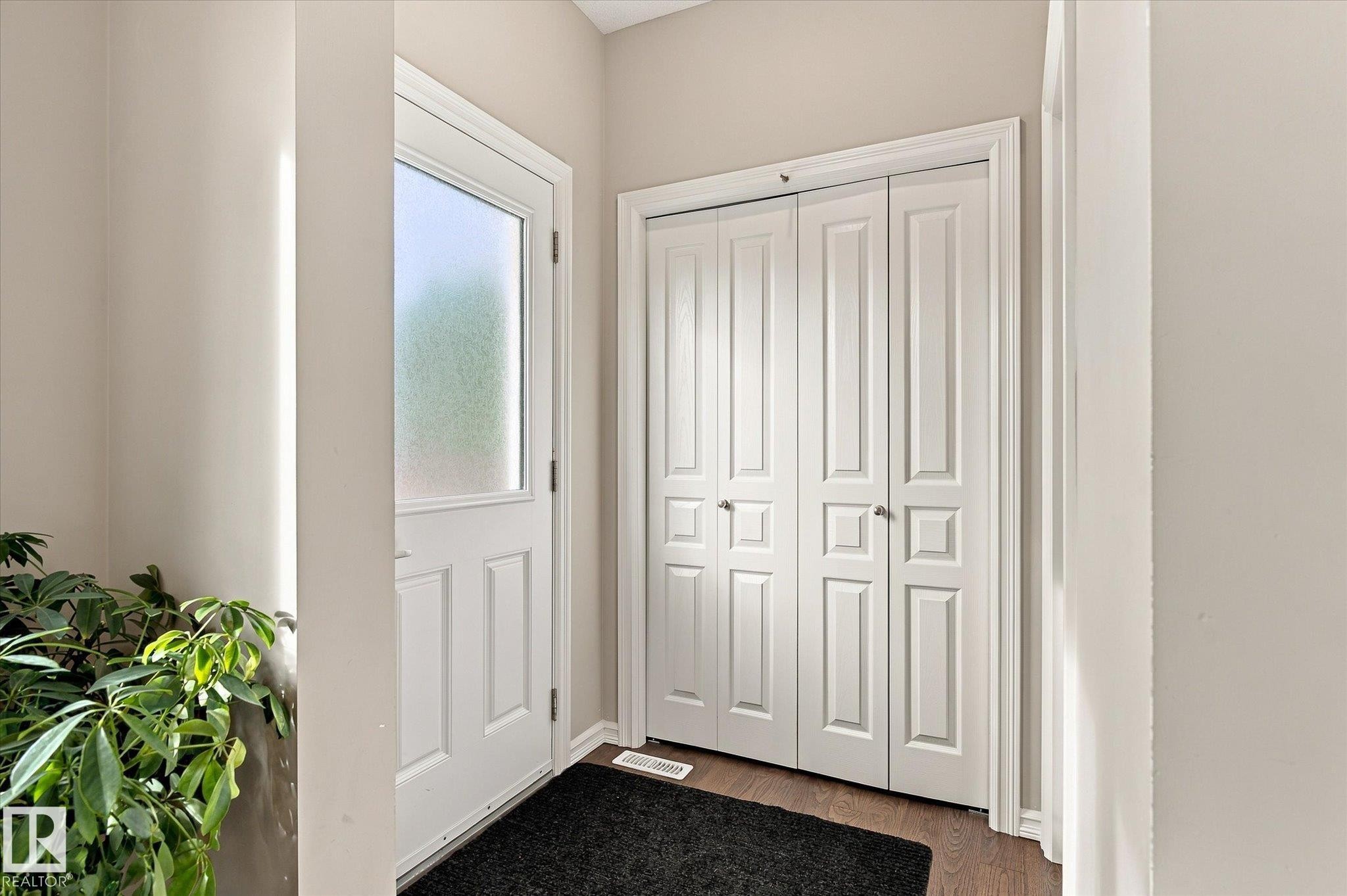 Entryway featuring a white paneled door with frosted glass, wood-finish flooring, and white bi-fold closet doors - 21935 91 Avenue Nw, Edmonton, AB