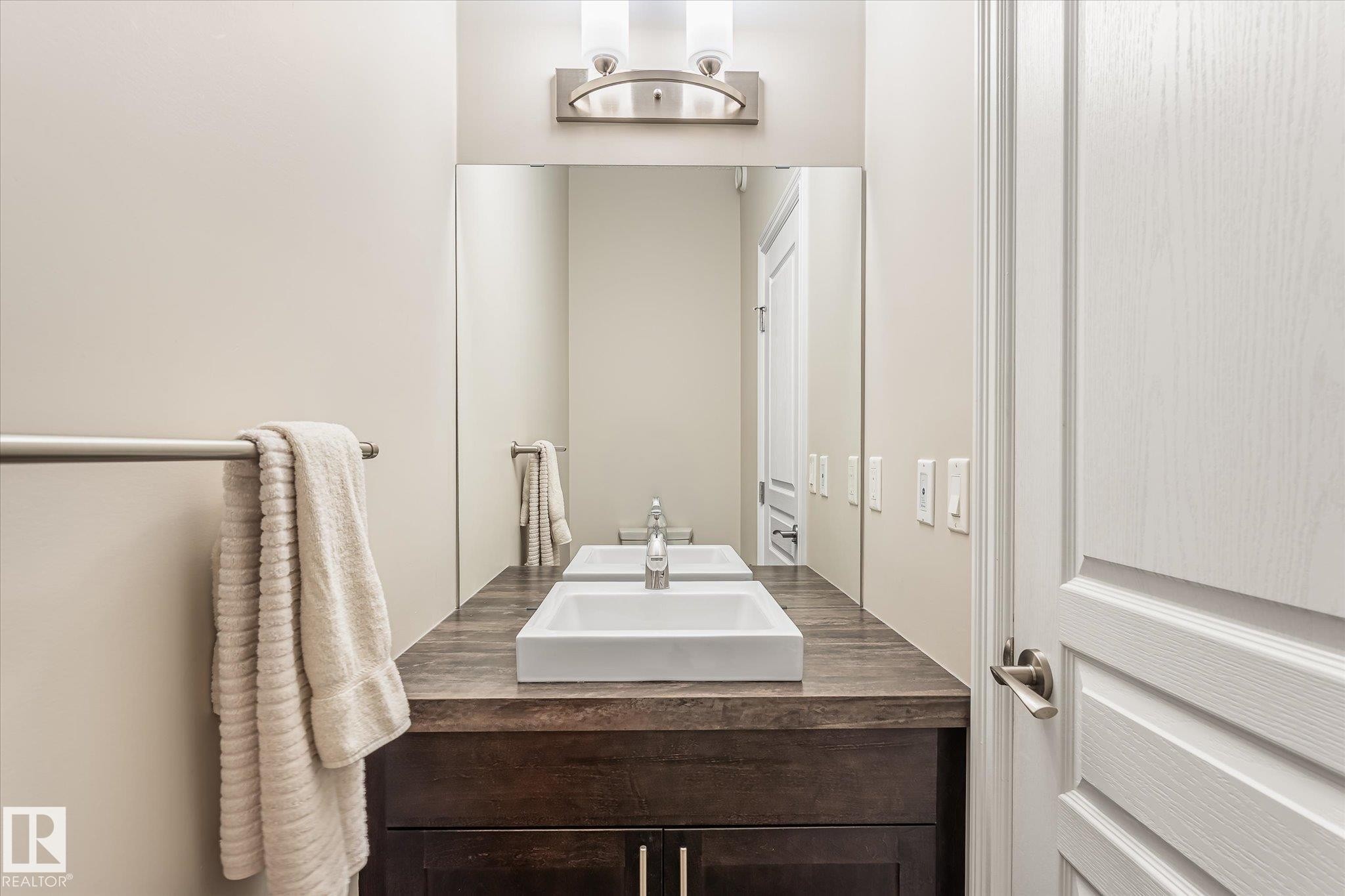 Wood-finish vanity with dual vessel sinks, full-width mirror, and wall-mounted light fixture - 21935 91 Avenue Nw, Edmonton, AB