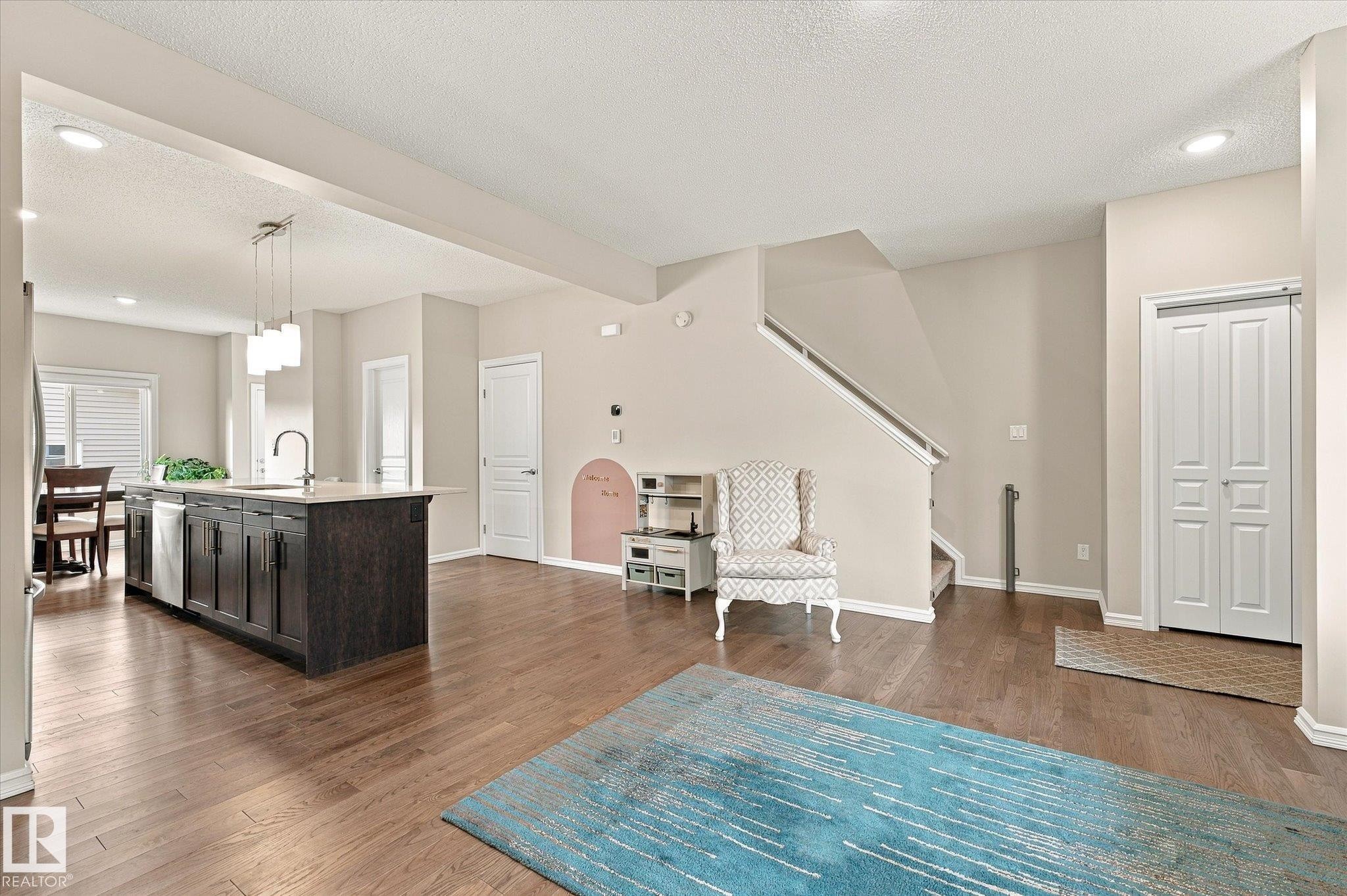 Open-concept living area featuring wood-finish flooring, recessed lighting, and a prominent kitchen island with a built-in sink and pendant lighting - 21935 91 Avenue Nw, Edmonton, AB