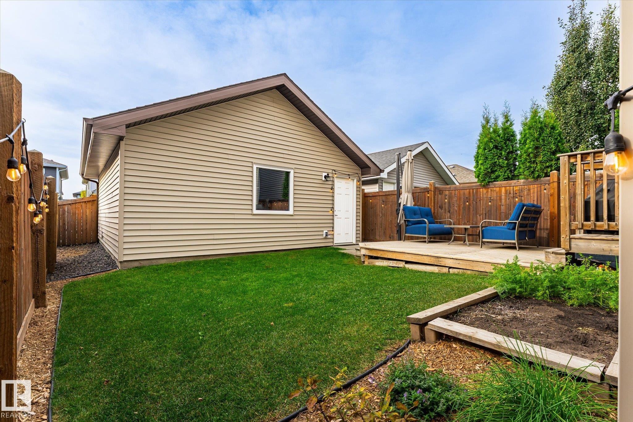 Expansive green lawn, elevated wood deck, wood privacy fencing, raised garden bed, and a detached building with horizontal siding - 21935 91 Avenue Nw, Edmonton, AB