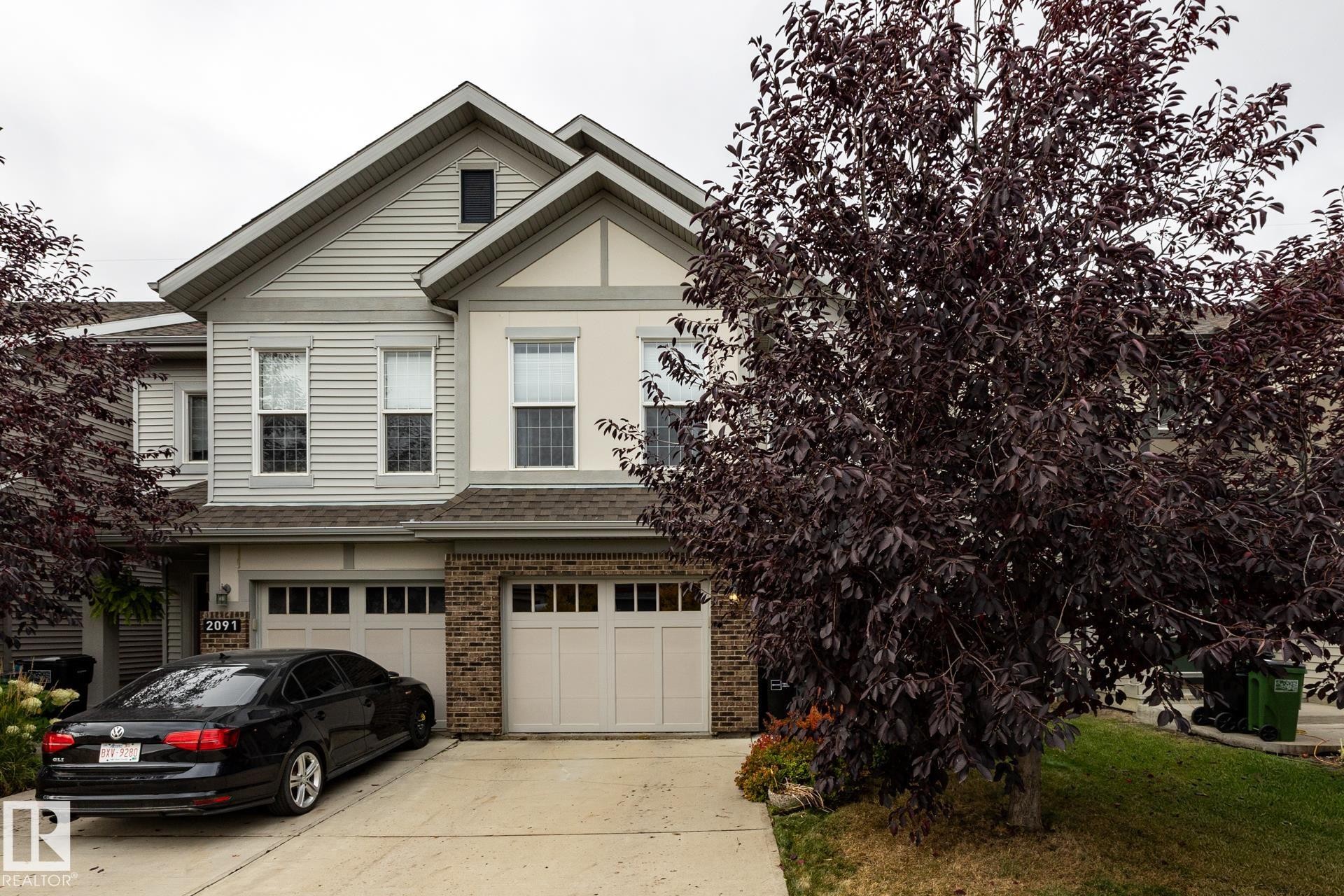 Multi-level exterior featuring horizontal siding, brick veneer accents, dual garage doors with glass panels, and a gabled roofline - 2093 Chalmers Way Sw, Edmonton, AB