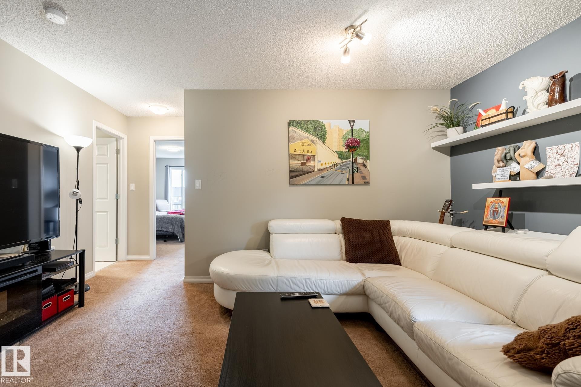 Living area featuring dual built-in wall shelving, an accent wall, multi-directional overhead track lighting, and neutral carpeting - 2093 Chalmers Way Sw, Edmonton, AB