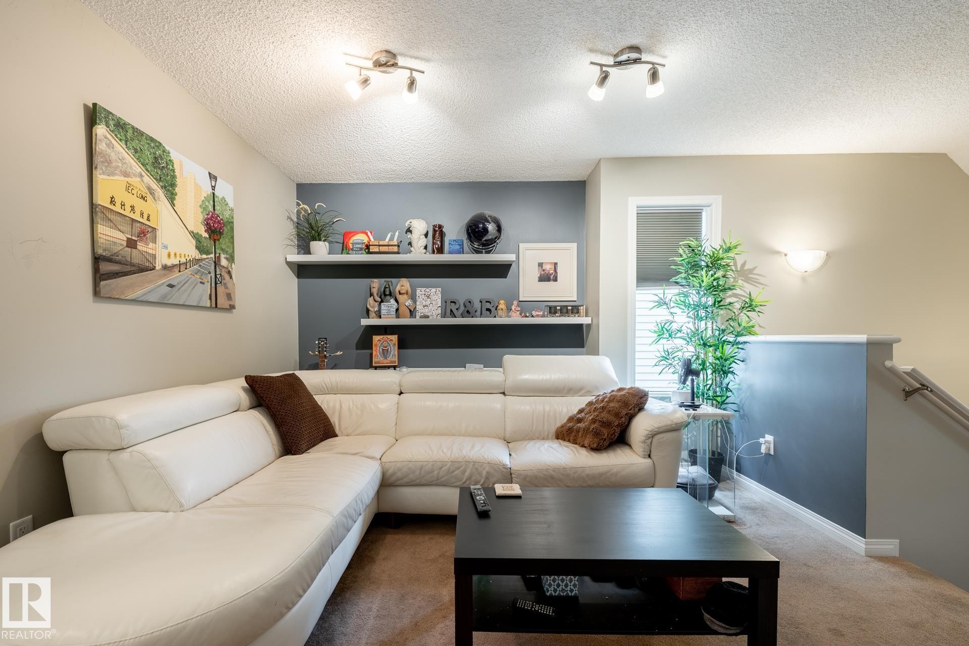 Accent wall featuring dual floating display shelves, multi-directional ceiling track lighting, wall-mounted sconce, and neutral carpeting - 2093 Chalmers Way Sw, Edmonton, AB