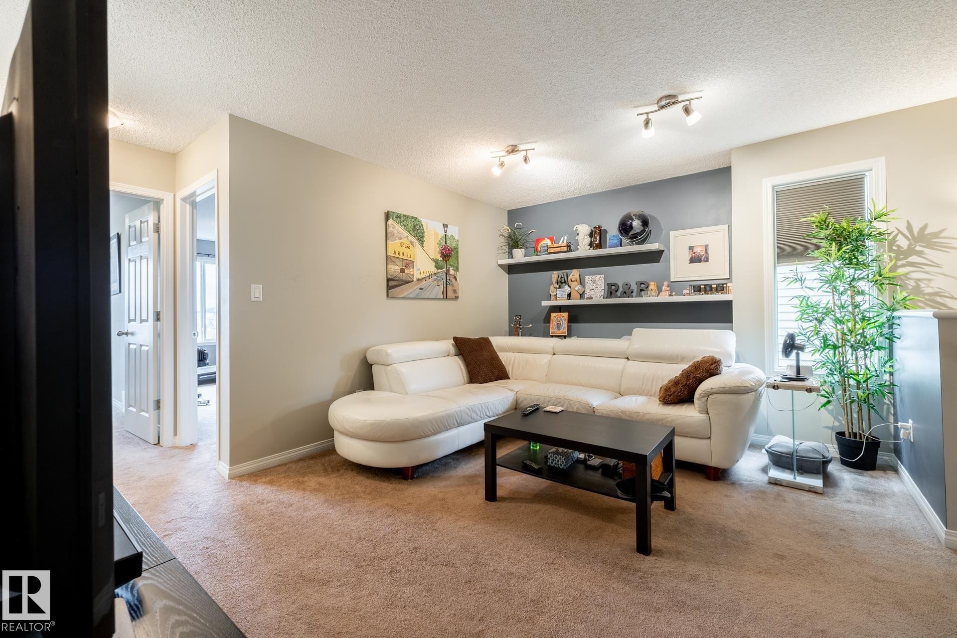 Living area featuring neutral wall tones, an accent wall with two built-in floating shelves, and dual track lighting fixtures - 2093 Chalmers Way Sw, Edmonton, AB