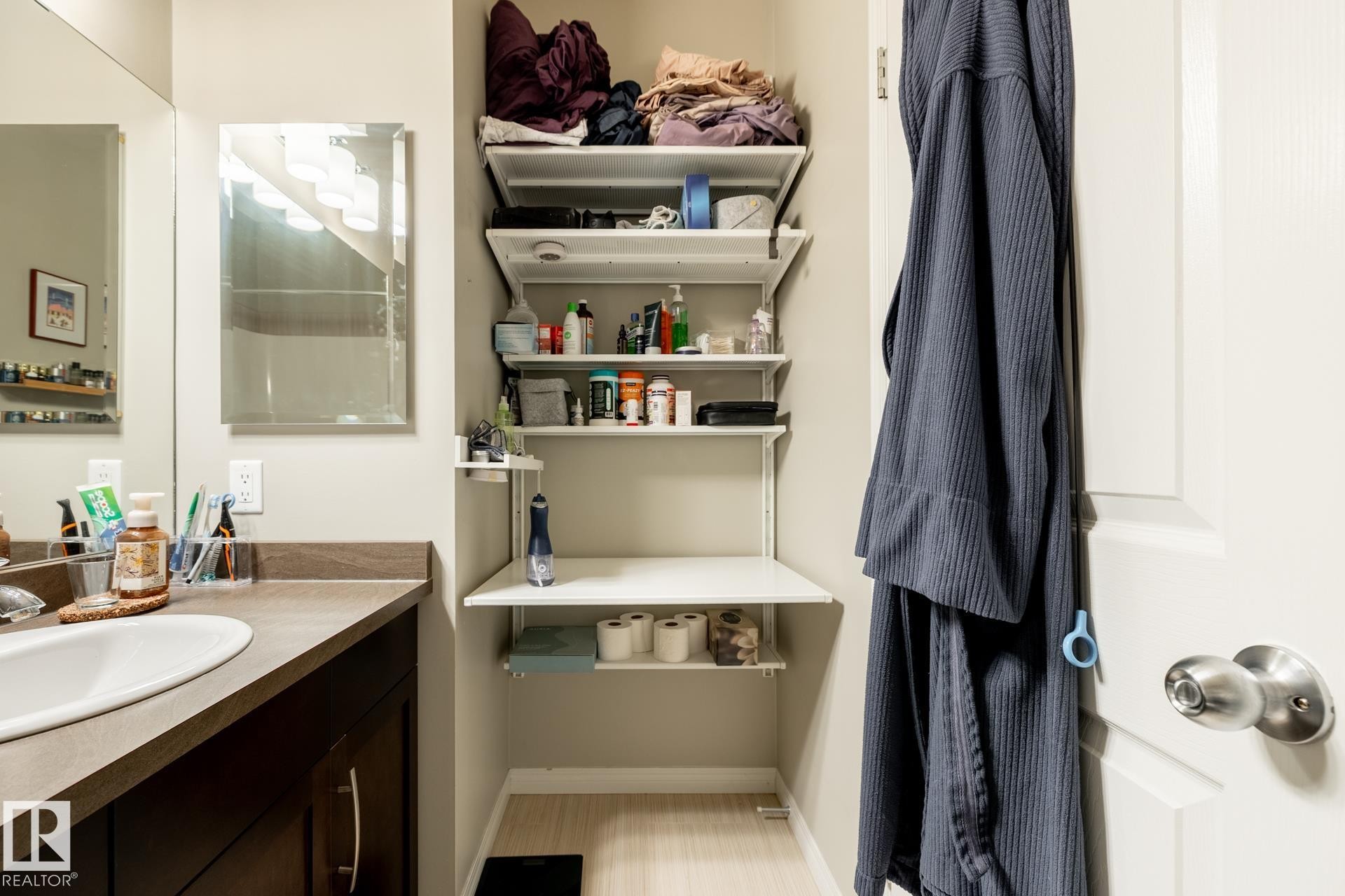 Bathroom featuring an oval drop-in sink, solid surface countertop, dark finish cabinetry with metal hardware, wall-mounted mirror, and adjustable white shelving system - 2093 Chalmers Way Sw, Edmonton, AB