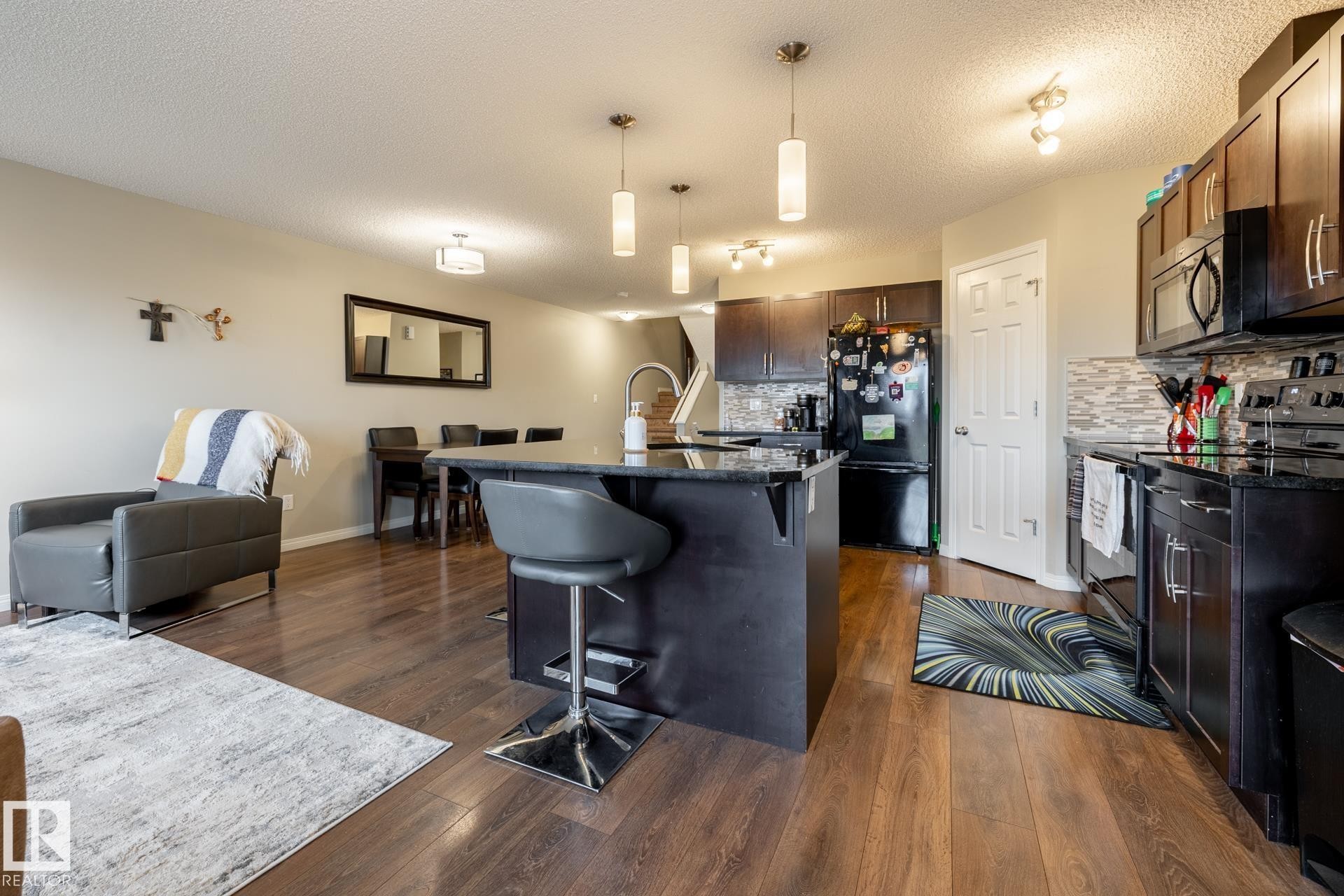 Kitchen featuring dark-toned cabinetry, a center island with a stone-finish countertop, wood-finish flooring, and multi-pendant lighting - 2093 Chalmers Way Sw, Edmonton, AB