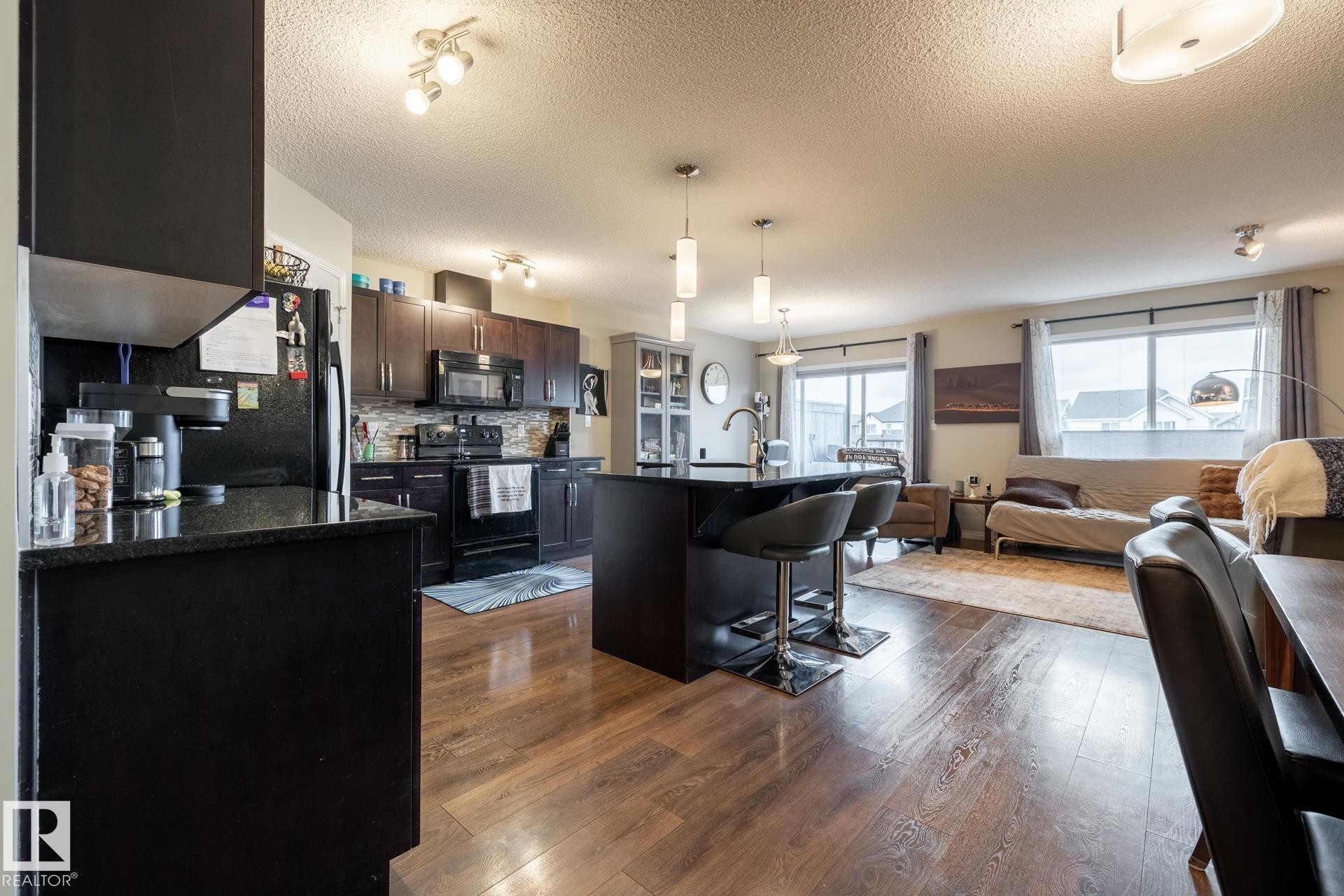 Kitchen featuring dark wood cabinetry, contrasting stone countertops, a central island with integrated seating, and wood-finish flooring - 2093 Chalmers Way Sw, Edmonton, AB