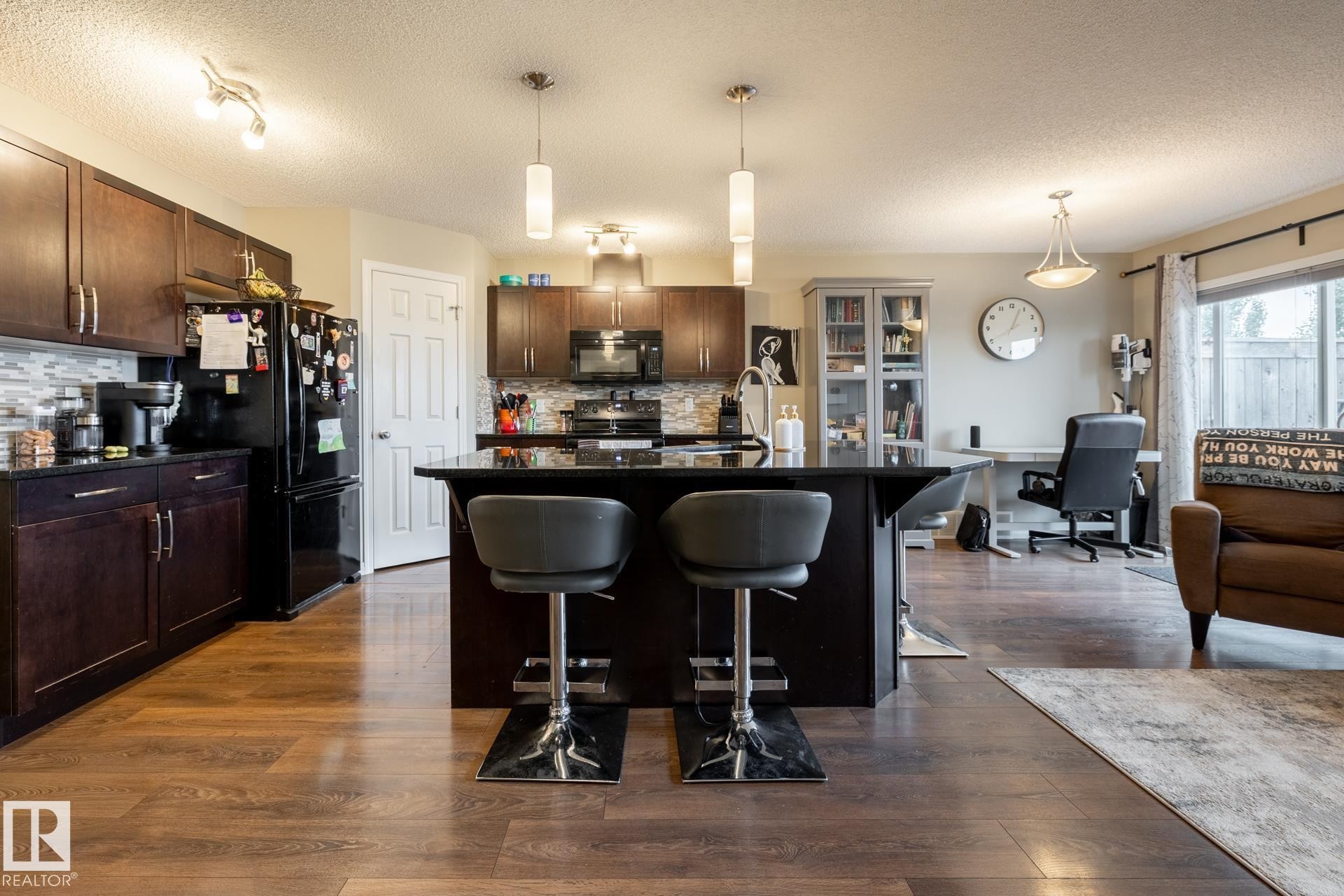 Kitchen featuring dark cabinetry, dark stone-topped center island, wood-finish flooring, glass-front built-in cabinetry, and pendant lighting - 2093 Chalmers Way Sw, Edmonton, AB