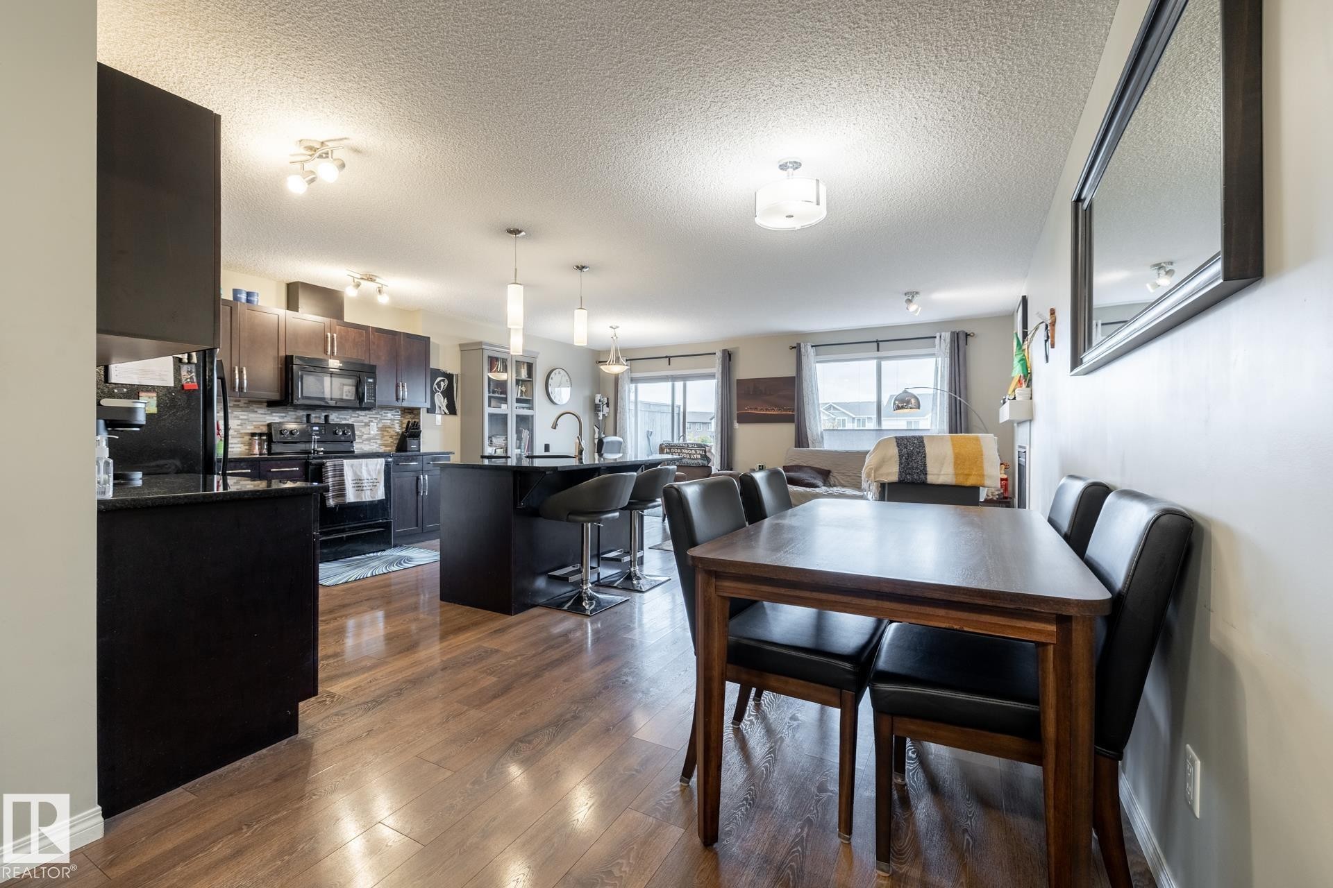 Kitchen featuring dark cabinetry, stone-finish countertops, a central island with pendant lighting, and wood-finish flooring - 2093 Chalmers Way Sw, Edmonton, AB