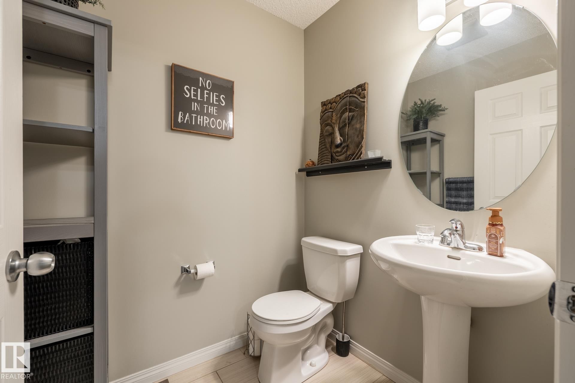Bathroom featuring a pedestal sink, oval wall-mounted mirror, three-light vanity fixture, and built-in shelving unit - 2093 Chalmers Way Sw, Edmonton, AB