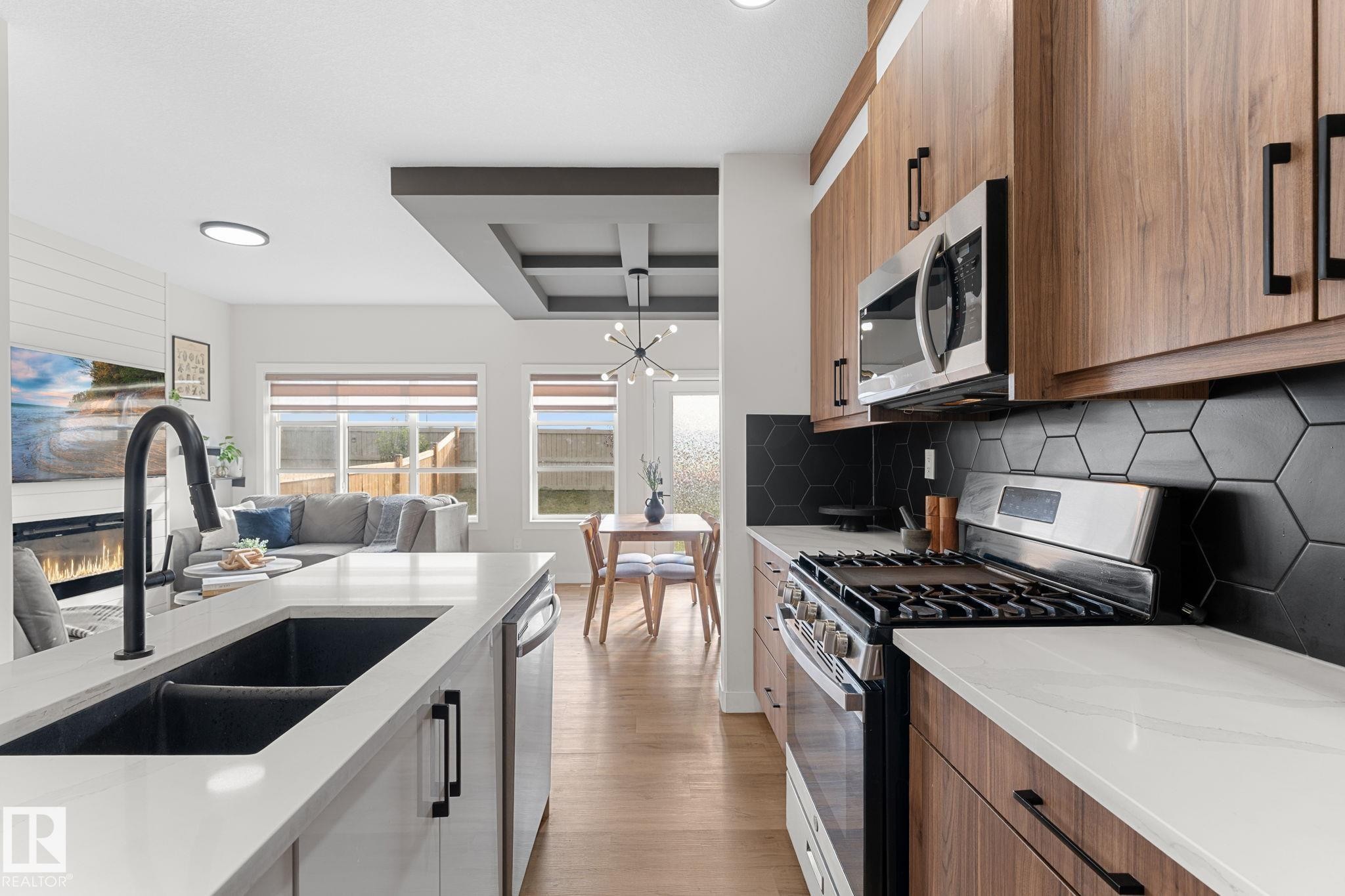 Kitchen with wood-finish cabinetry, stainless steel appliances, white countertops, a dark hexagonal tile backsplash, and a built-in sink with a black fixture - 1142 Goldfinch Crescent Nw, Edmonton, AB