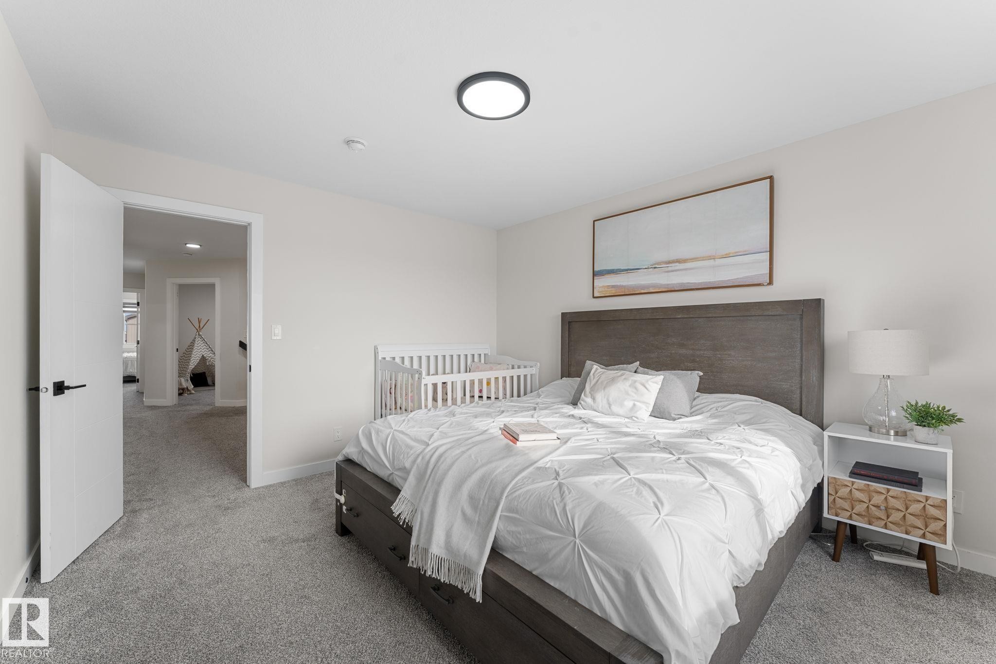 Spacious bedroom featuring light neutral wall tones, grey carpeting, a flush-mount ceiling light, and a solid wood headboard - 1142 Goldfinch Crescent Nw, Edmonton, AB