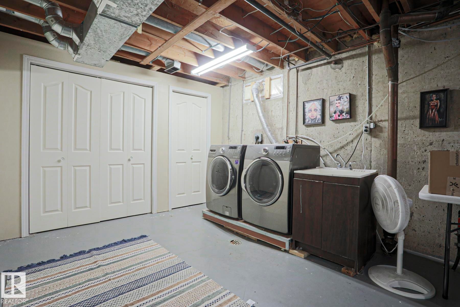 Dedicated laundry area featuring a utility sink and cabinetry, two bi-fold doors, and exposed ceiling joists - 5 Gilmore Crescent, St. Albert, AB