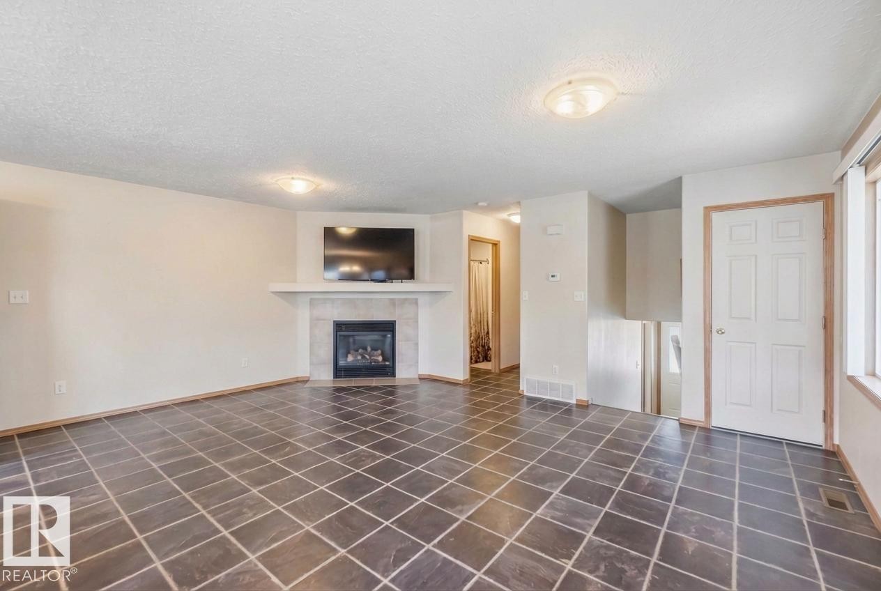 Spacious open-concept living area featuring large-format tile flooring set on a diagonal, neutral wall tones, and recessed ceiling lighting - 497 Kananaskis Drive, Devon, AB