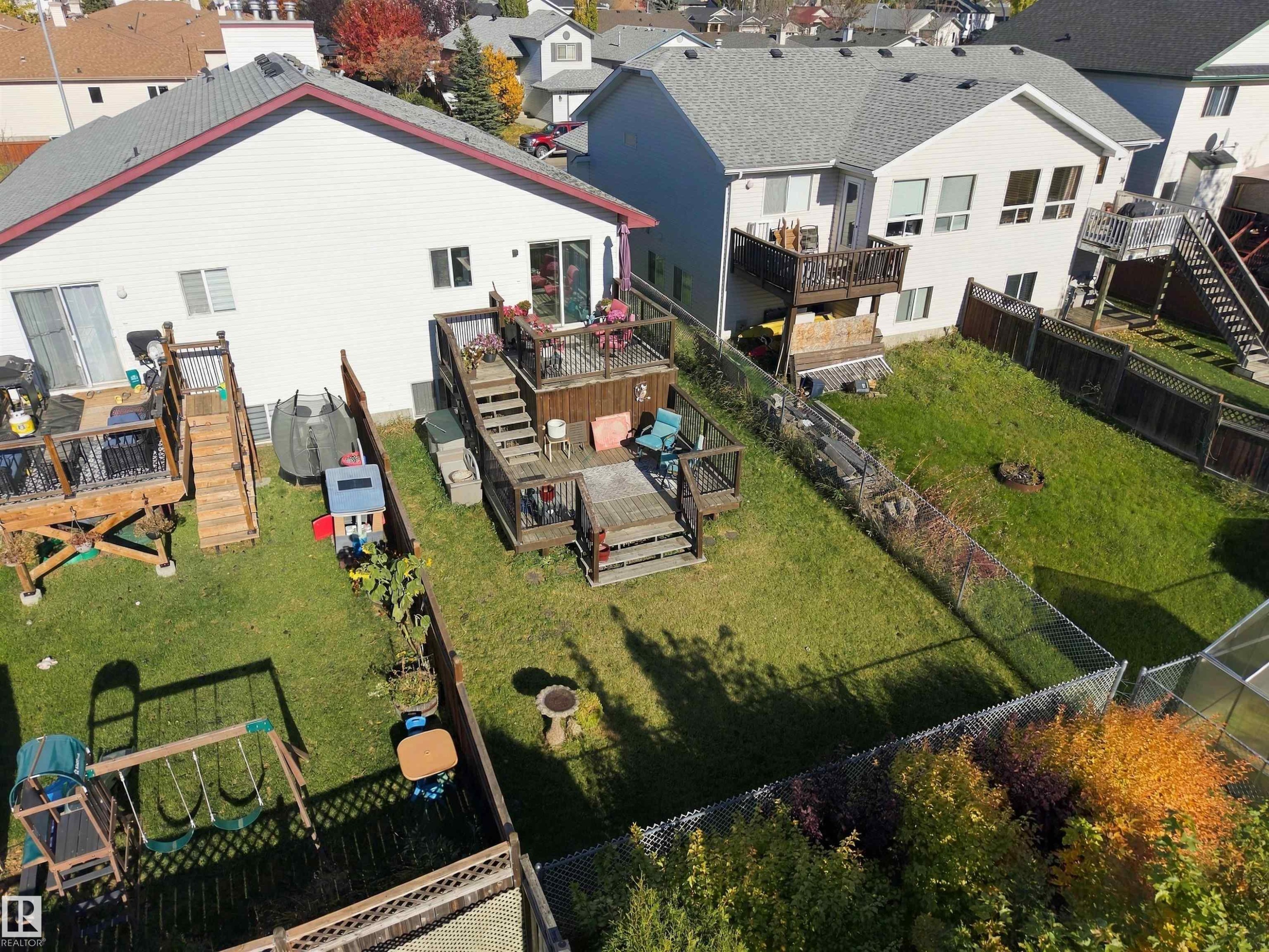 Multi-level wood deck featuring integrated railings and stair access, chain-link perimeter fencing, and a grass lawn - 497 Kananaskis Drive, Devon, AB