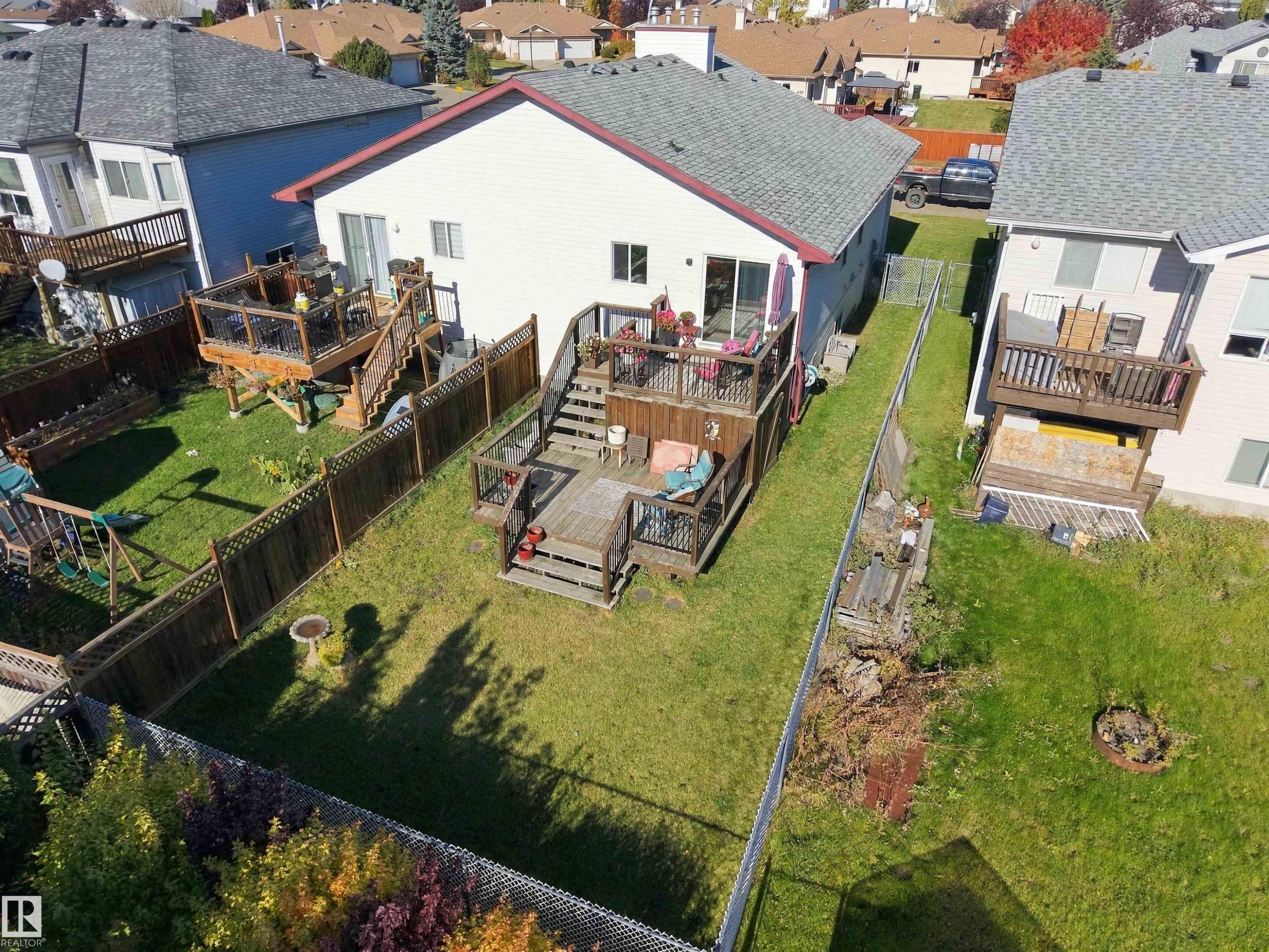 Multi-level wood deck featuring black metal railings, lattice privacy screening, and stairs leading to a backyard lawn - 497 Kananaskis Drive, Devon, AB