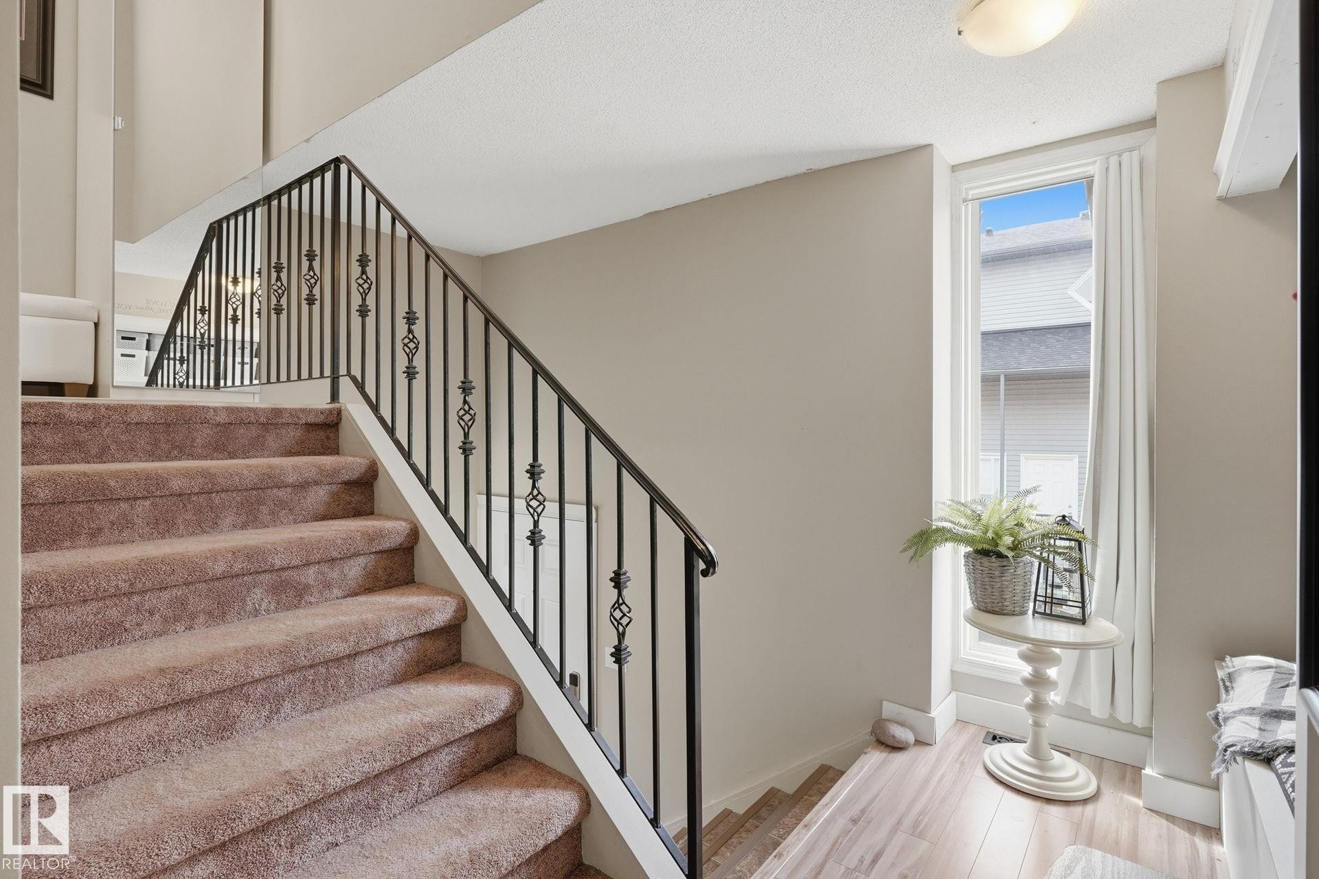 Carpeted staircase with wrought iron railing, neutral wall color, and wood-finish flooring - 5340 38A Avenue Nw, Edmonton, AB