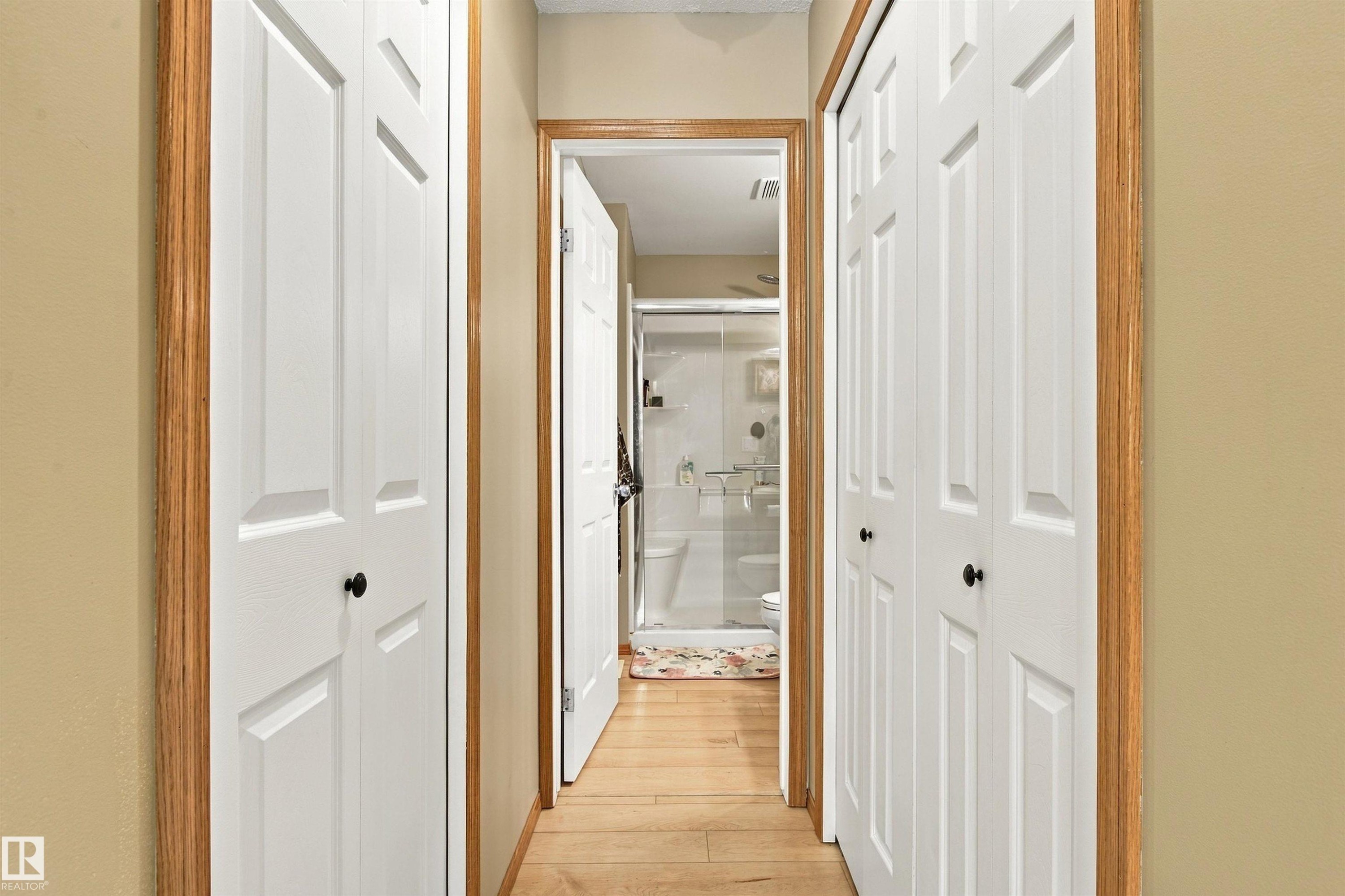 Hallway with wood-finish flooring, light-colored walls, and white bi-fold closet doors with black hardware - 51064 Rge Rd 222, Rural Strathcona County, AB