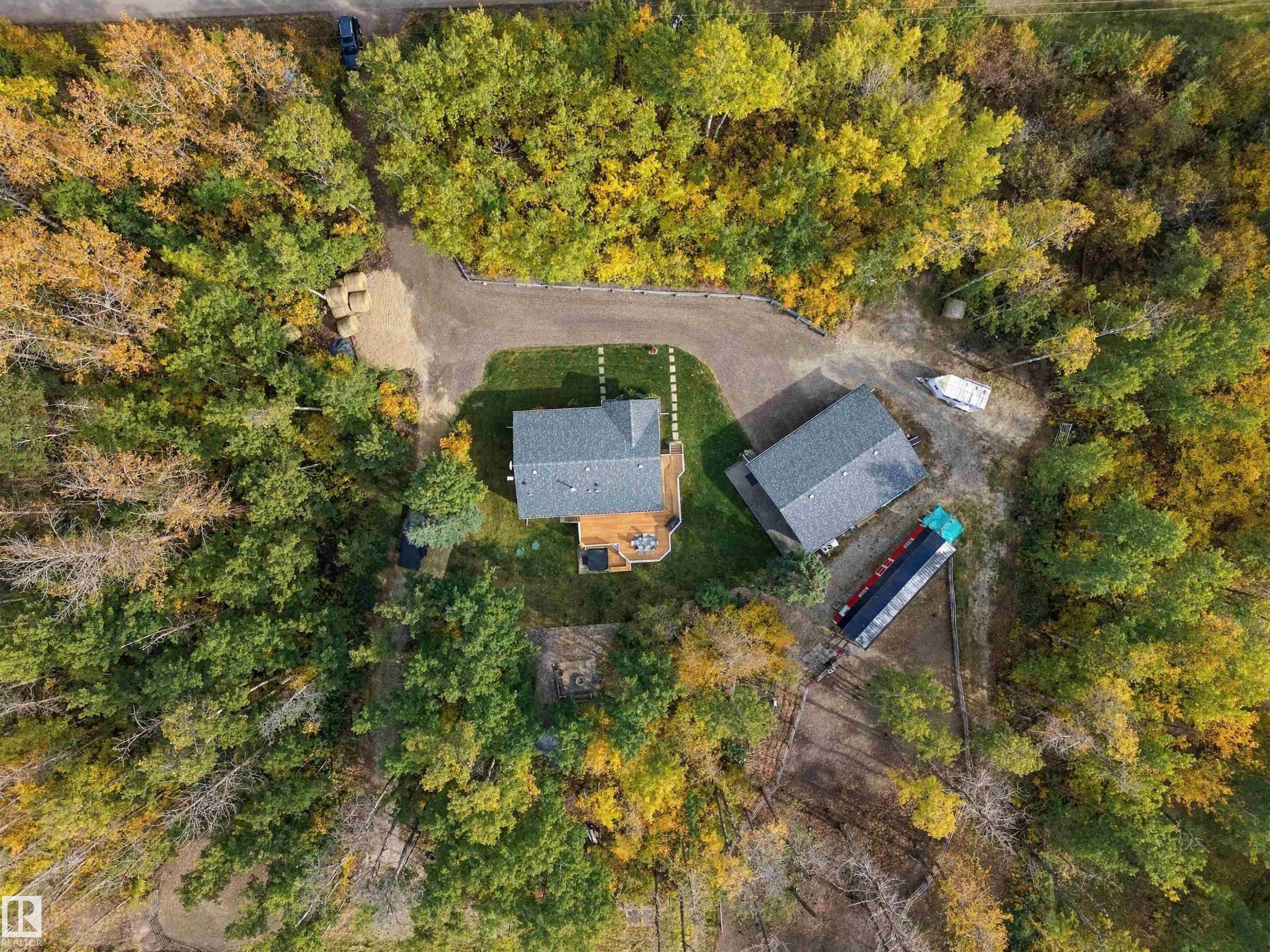 Private, treed parcel featuring a primary residence with a deck, a detached outbuilding, and a gravel driveway - 51064 Rge Rd 222, Rural Strathcona County, AB