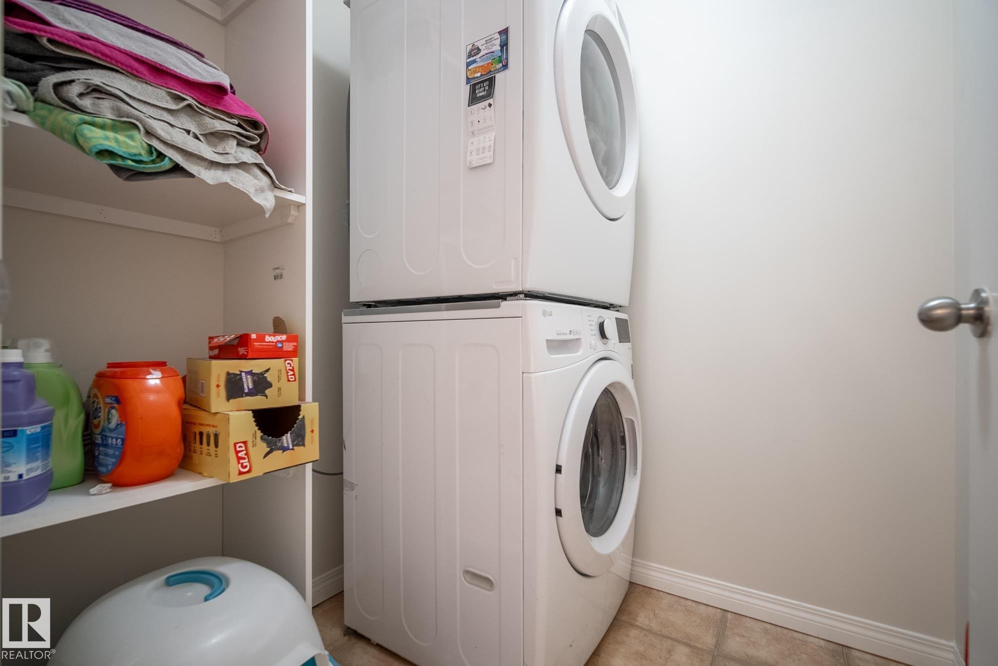 Stacked washer and dryer unit, built-in shelving, and neutral wall paint - #416 111 Edwards Dr Sw, Edmonton, AB