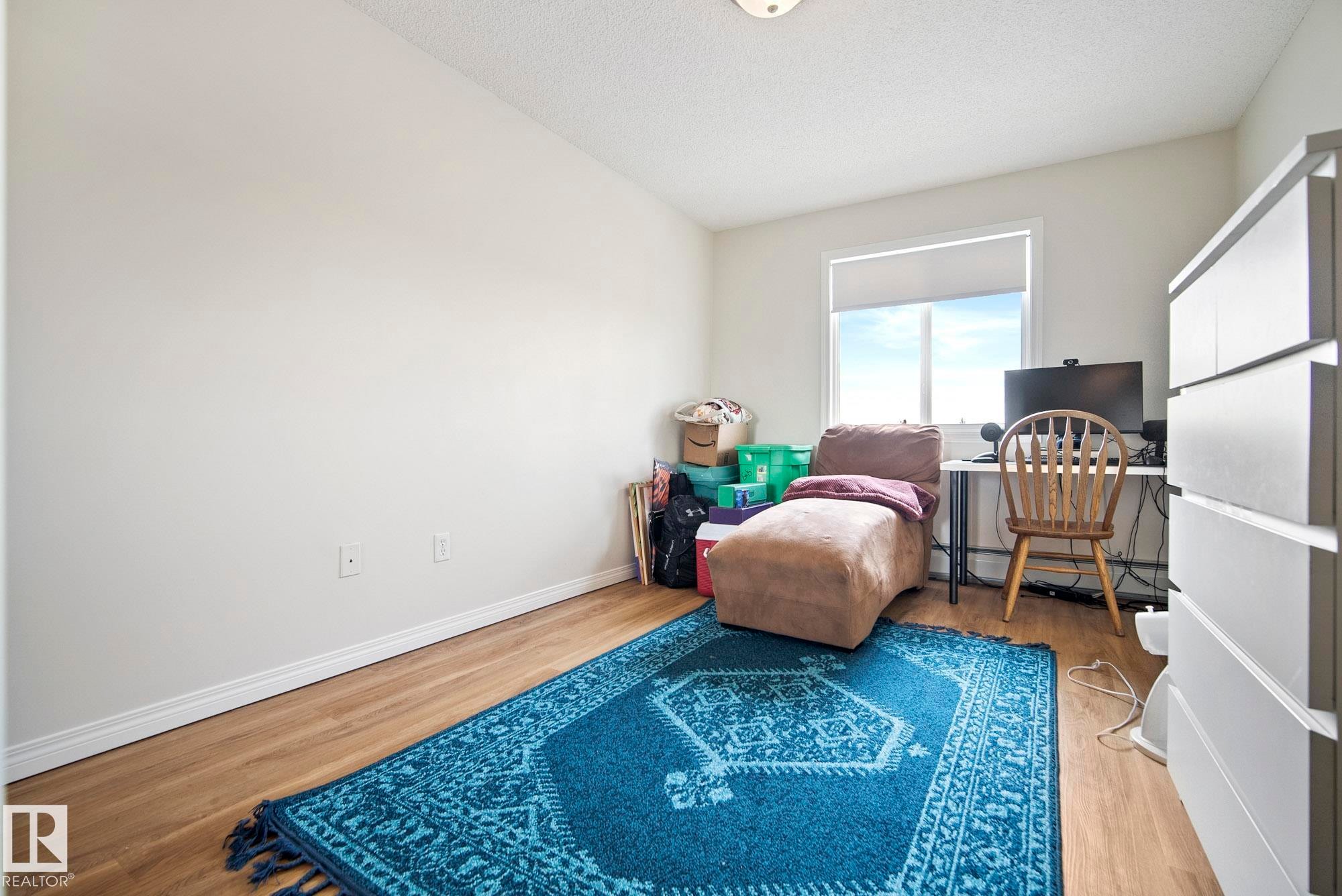 Wood-finish flooring with white baseboards, bright white walls, and a window with a roller shade - #416 111 Edwards Dr Sw, Edmonton, AB