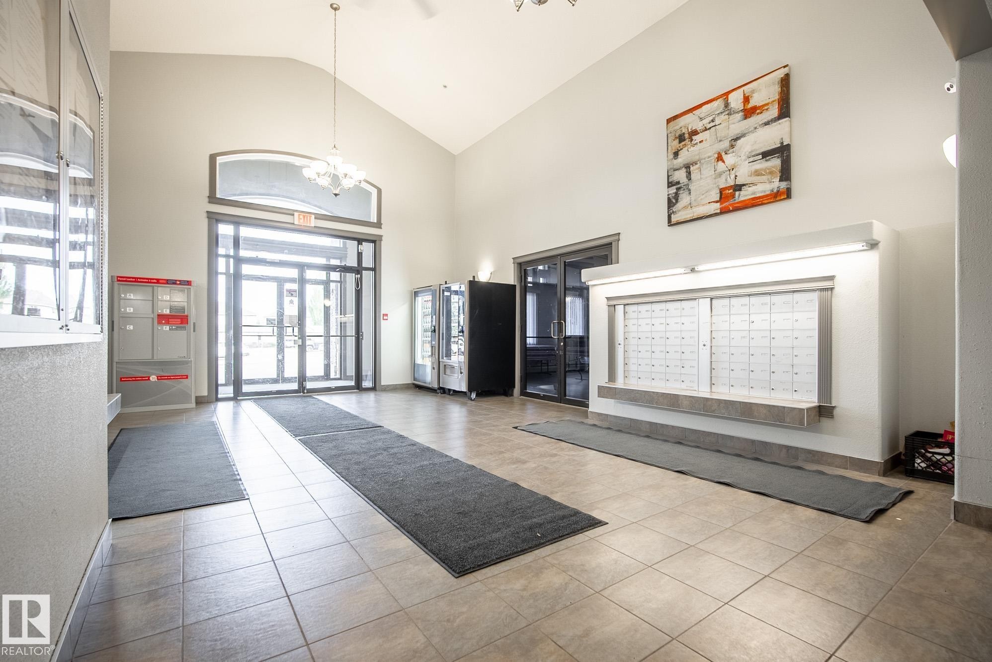 Spacious entryway featuring a vaulted ceiling, durable tile flooring, and integrated wall-mounted mailboxes - #416 111 Edwards Dr Sw, Edmonton, AB
