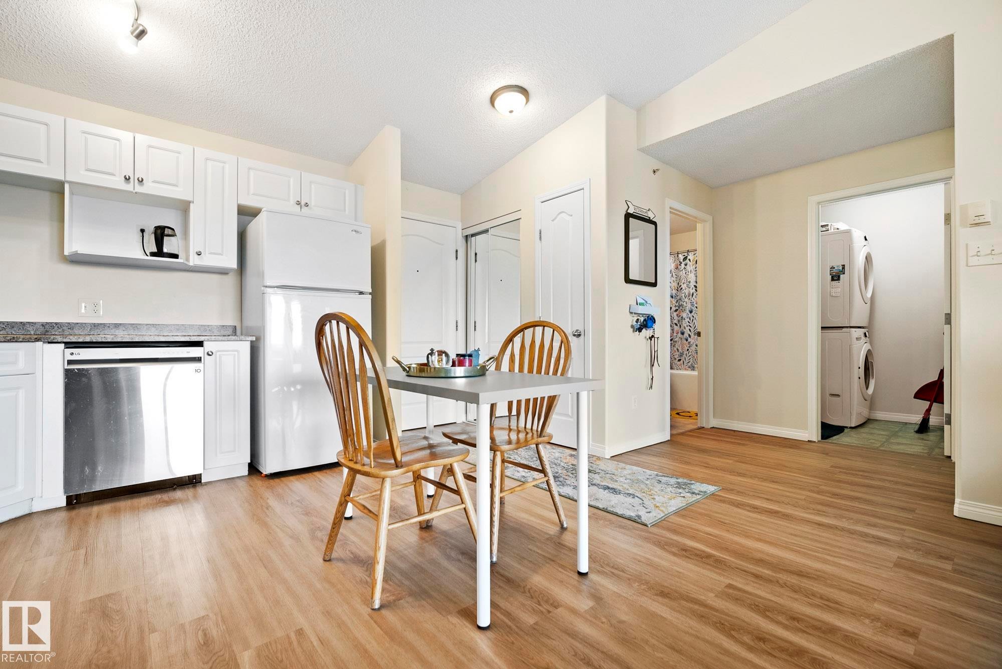 Kitchen featuring white cabinetry, stainless steel dishwasher, and wood-finish flooring - #416 111 Edwards Dr Sw, Edmonton, AB
