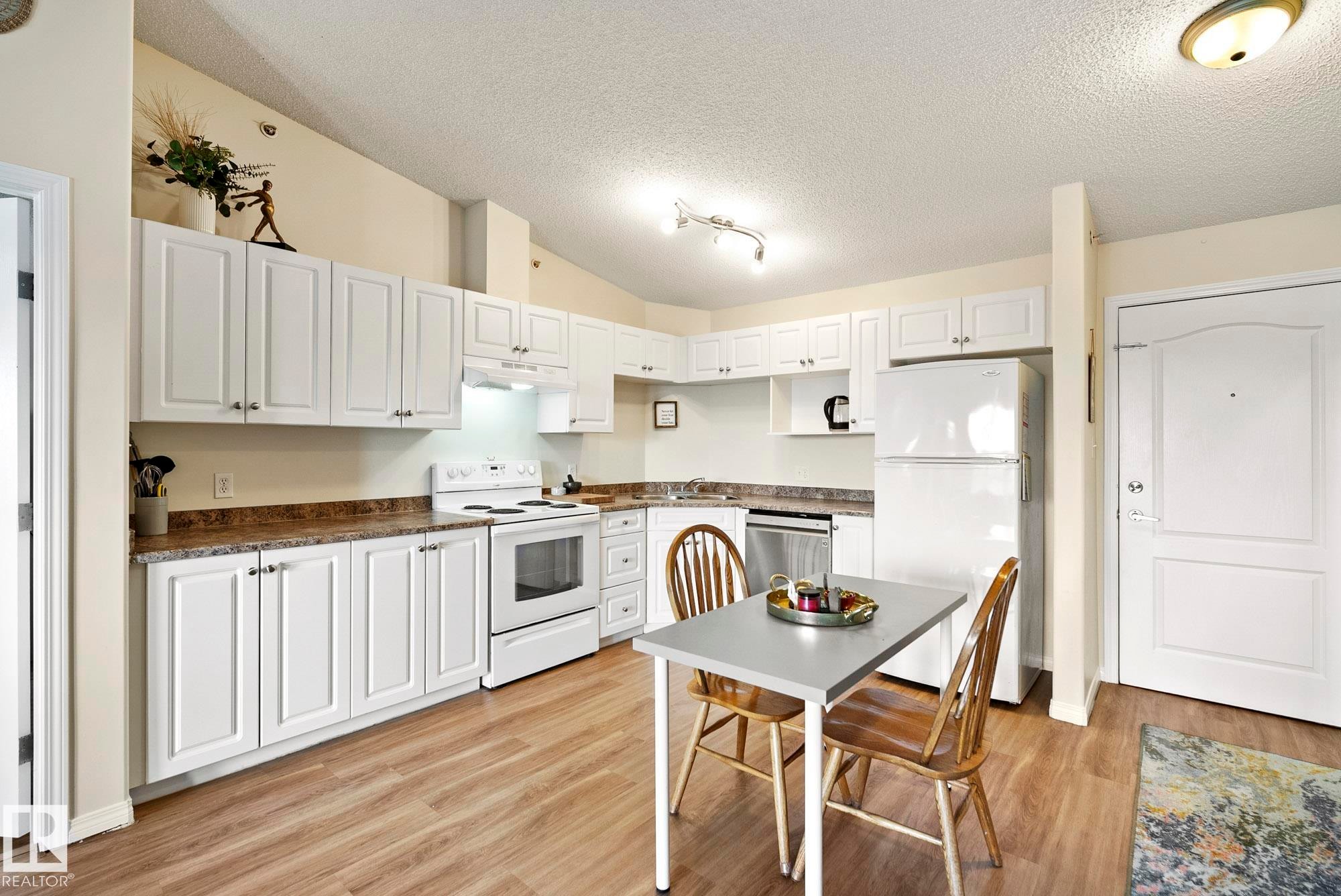 Kitchen featuring white cabinetry, wood-finish flooring, white appliances, and a built-in dishwasher - #416 111 Edwards Dr Sw, Edmonton, AB