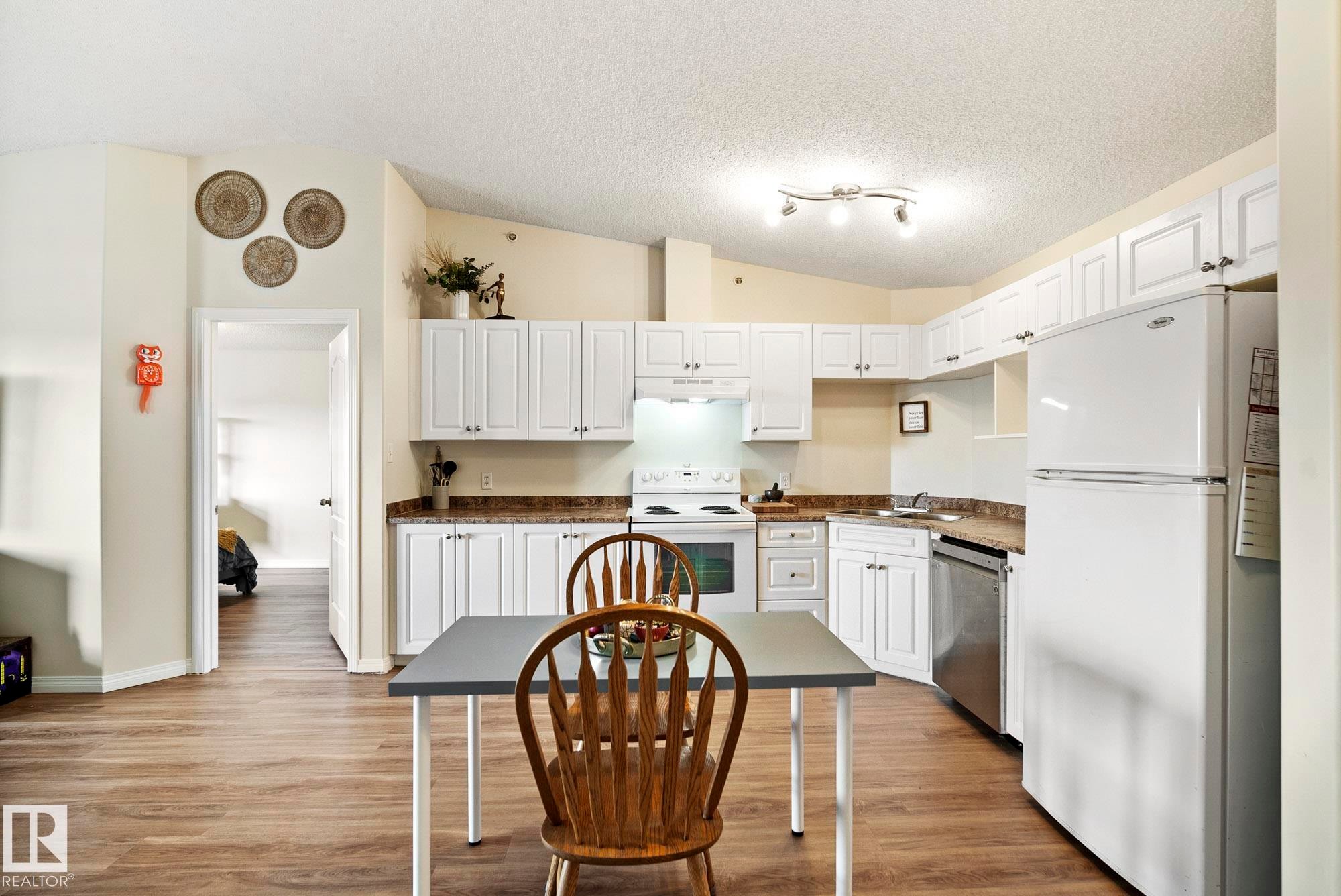 White cabinetry, wood-finish flooring, white appliances, track lighting, and a composite countertop - #416 111 Edwards Dr Sw, Edmonton, AB