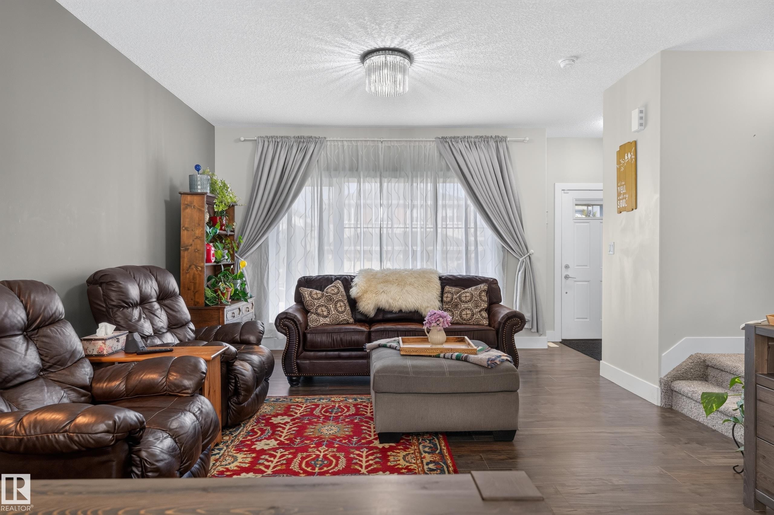 Living space featuring wood-finish flooring, a neutral color palette, a flush-mount crystal chandelier, and a large window with natural light - 798 Berg Loop, Leduc, AB