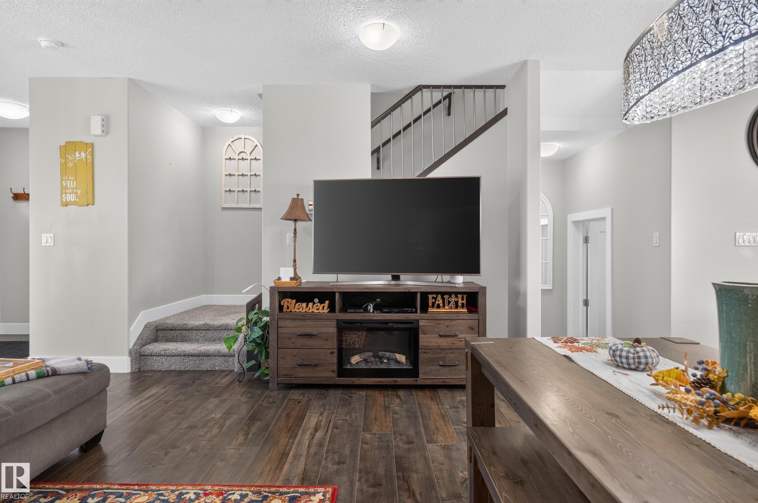 Wood-finish flooring, staircase with metal balusters, and drum-style chandelier with decorative detailing - 798 Berg Loop, Leduc, AB