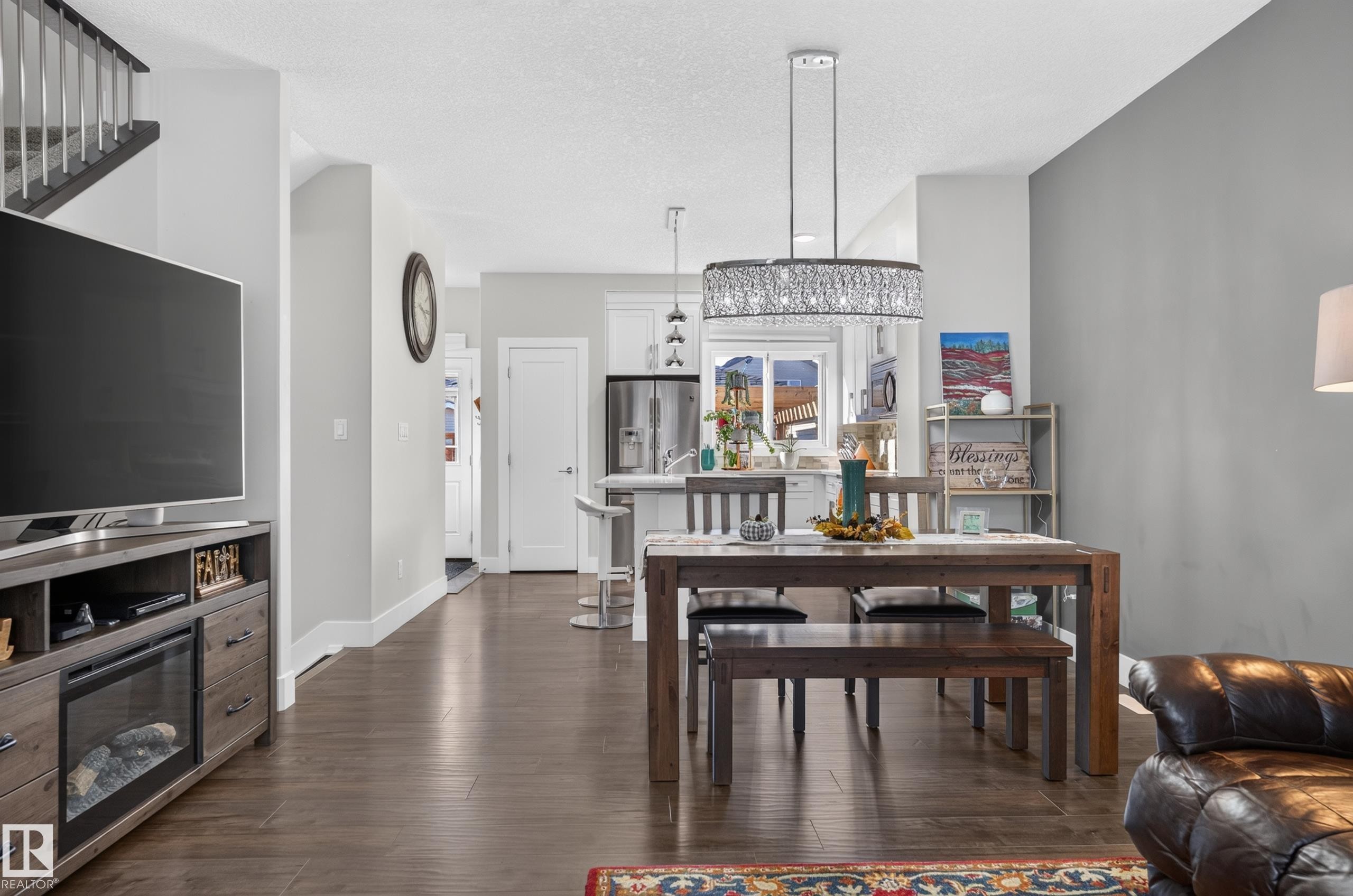 Open-concept interior featuring wood-finish flooring, a tiered drum pendant light with crystal accents, white cabinetry, and a kitchen island - 798 Berg Loop, Leduc, AB
