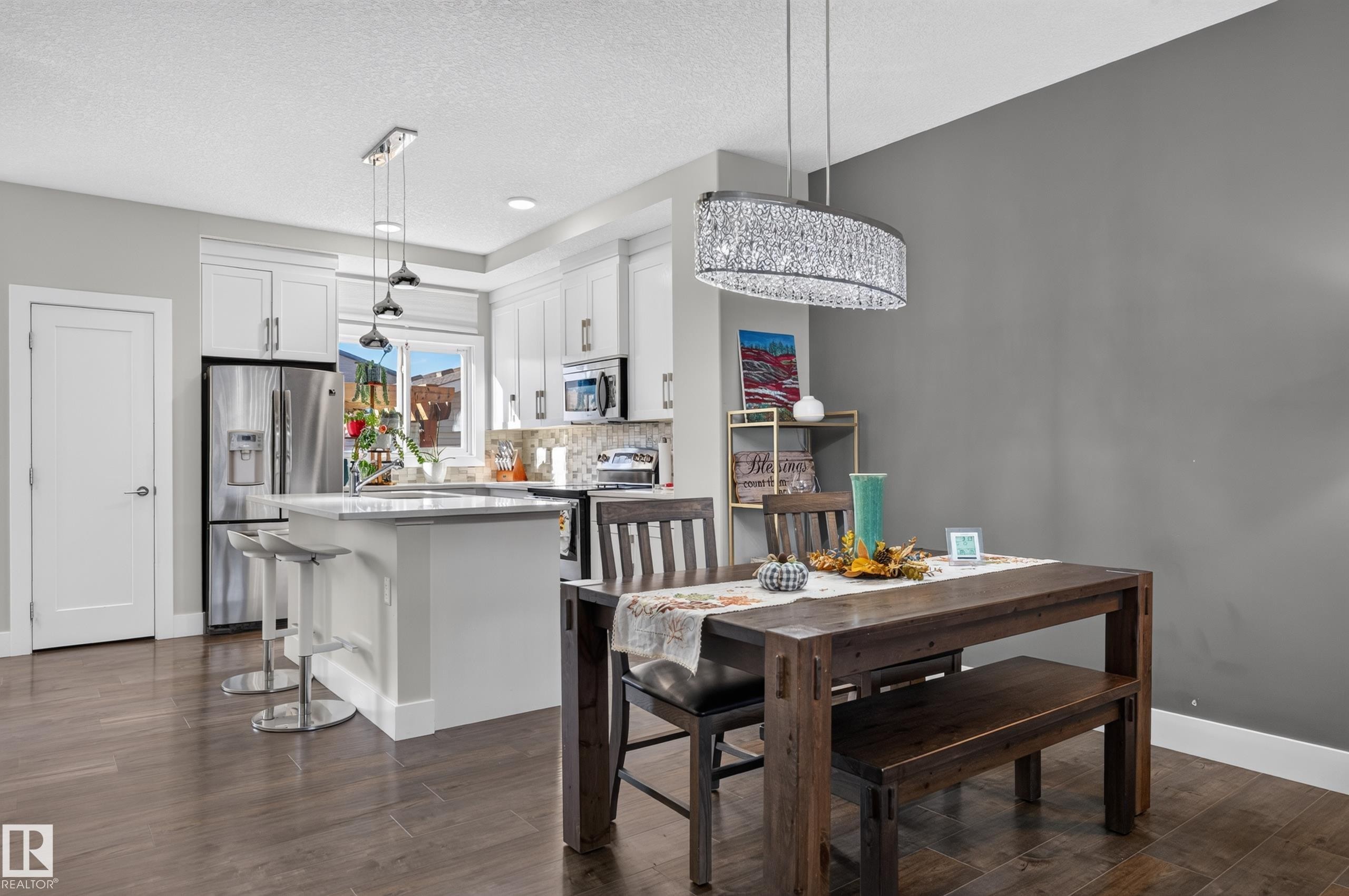 Kitchen featuring white cabinetry, an island with stone-composite countertop, wood-finish flooring, and a crystal-accented linear pendant light fixture - 798 Berg Loop, Leduc, AB