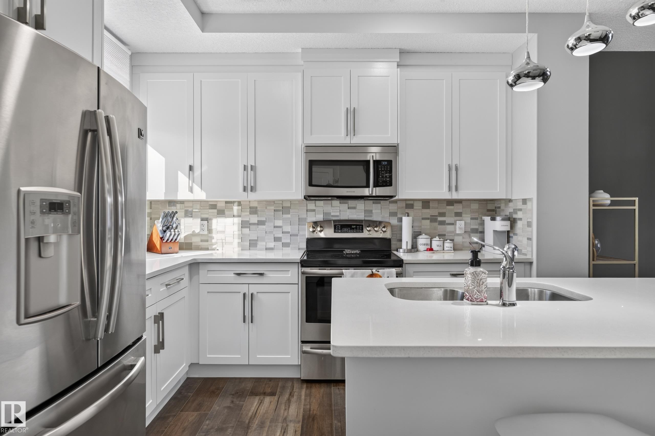 Kitchen featuring white cabinetry, quartz countertops, stainless steel appliances, multi-toned mosaic tile backsplash, and wood-finish flooring - 798 Berg Loop, Leduc, AB