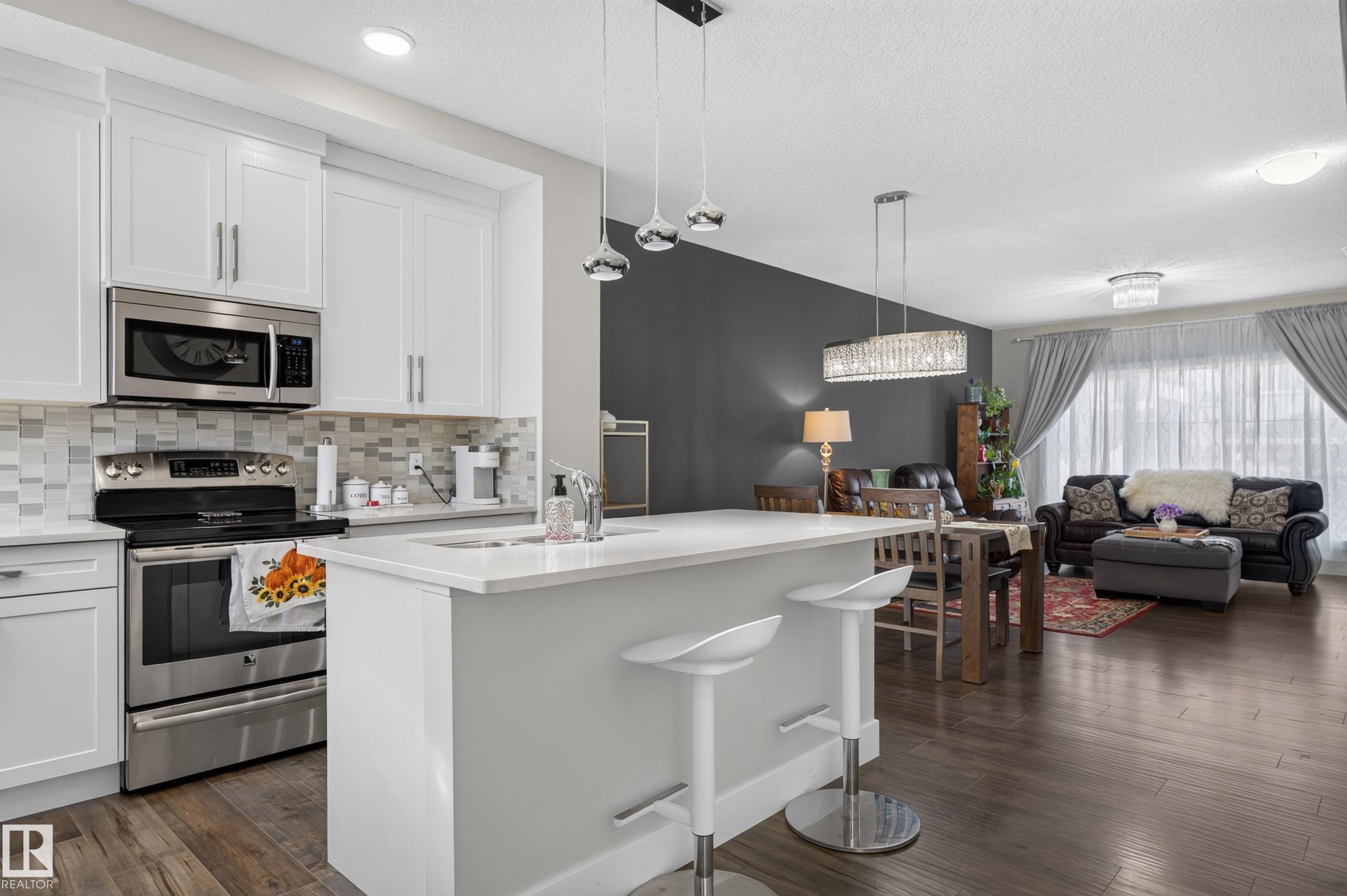 Kitchen featuring white cabinetry, stone-finish countertops, stainless steel appliances, multi-toned tile backsplash, and wood-finish flooring - 798 Berg Loop, Leduc, AB