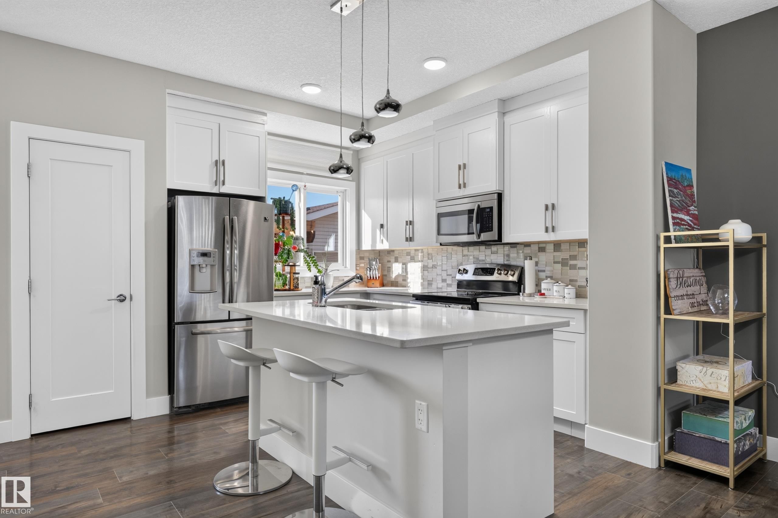 Kitchen featuring white cabinetry, quartz countertops, a central island with a stainless steel sink, tile backsplash, and stainless steel appliances - 798 Berg Loop, Leduc, AB