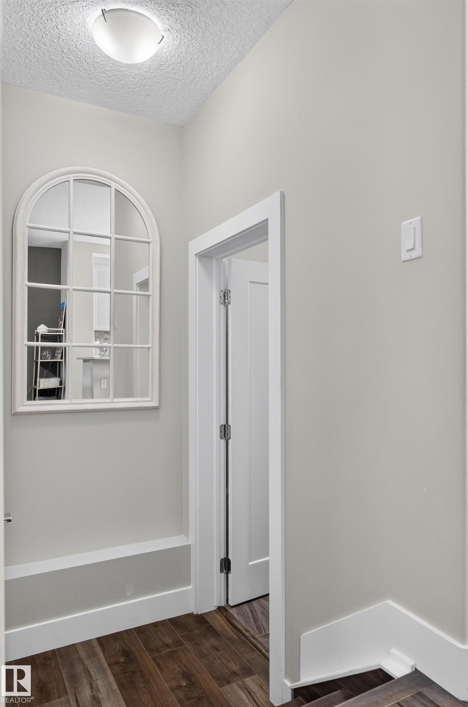 Neutral-toned interior featuring wood-finish flooring, an arched window-pane wall mirror with white trim, and a solid-core interior door with a shaker-style design - 798 Berg Loop, Leduc, AB