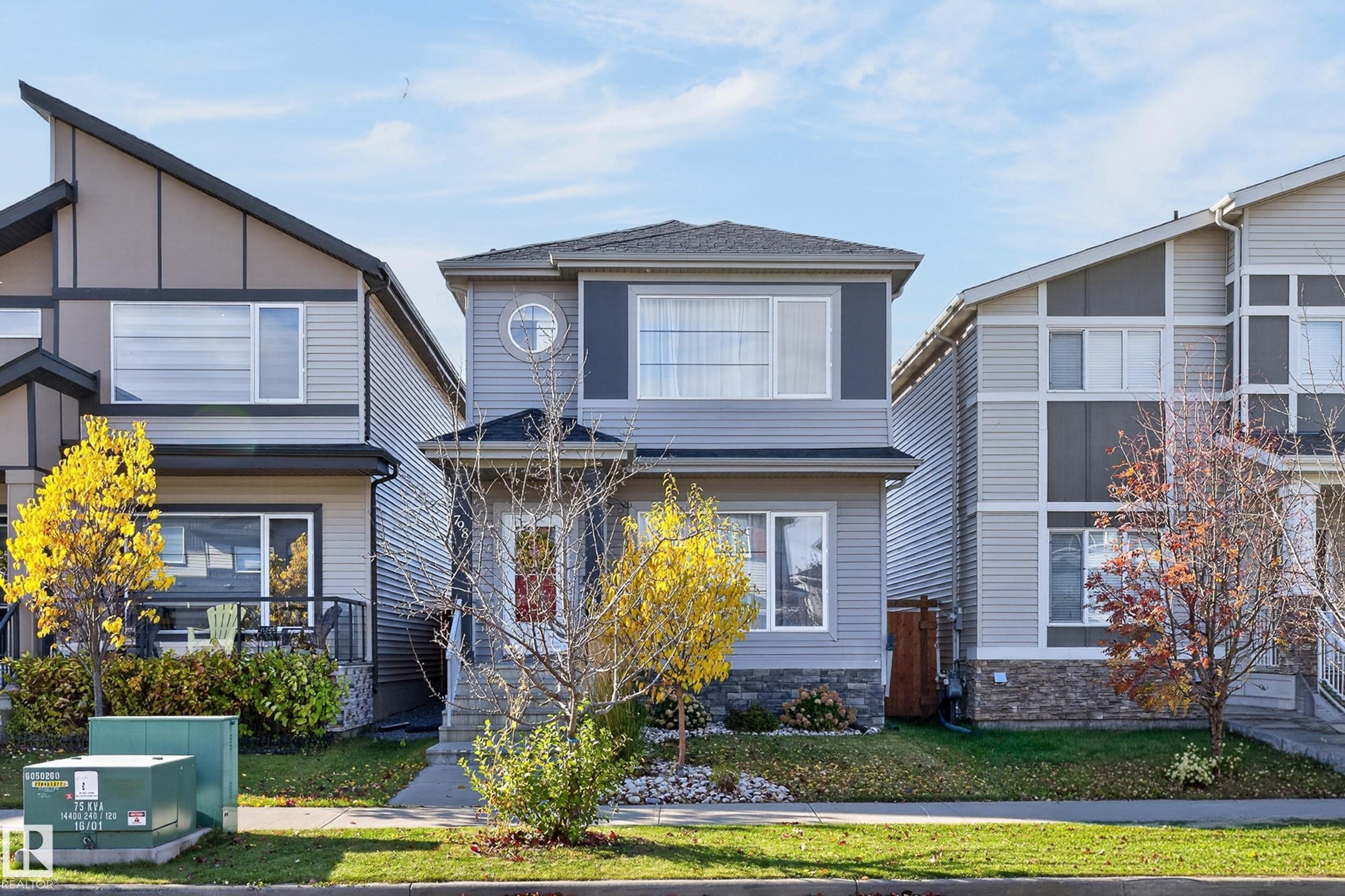 Multi-level exterior featuring horizontal lap siding, stone veneer accents, a decorative circular window, and a covered front entryway - 798 Berg Loop, Leduc, AB