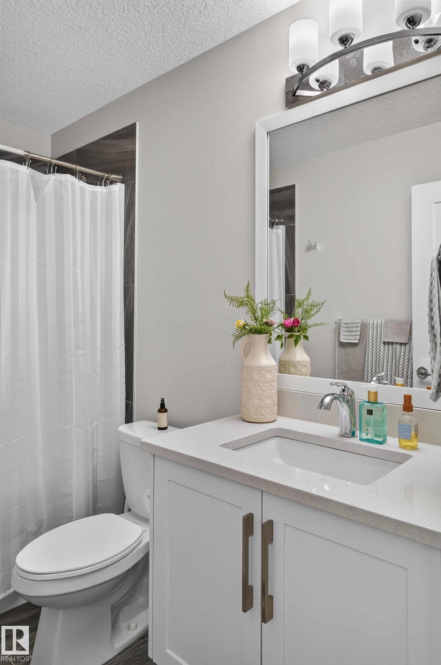 White vanity with a neutral solid-surface countertop, rectangular undermount sink, brushed metal hardware, and a multi-bulb light fixture above a framed mirror - 798 Berg Loop, Leduc, AB