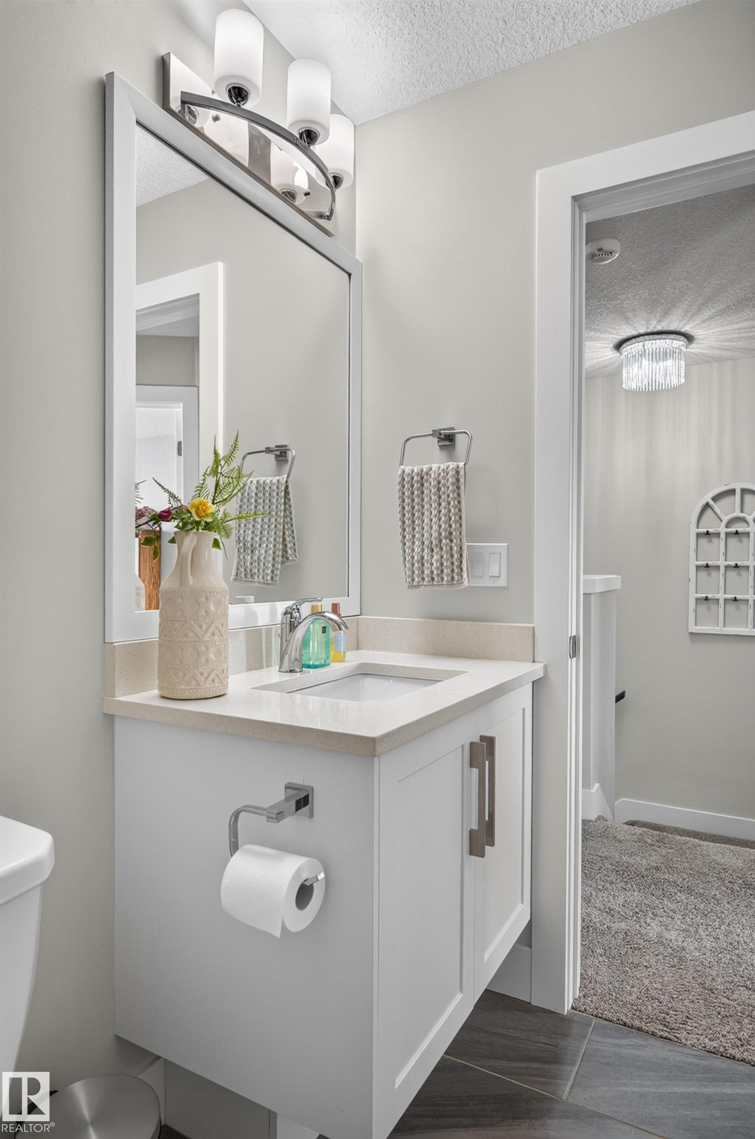 White vanity featuring a solid surface countertop, integrated rectangular basin, brushed nickel hardware, and a three-light wall-mounted fixture with a matching framed mirror - 798 Berg Loop, Leduc, AB